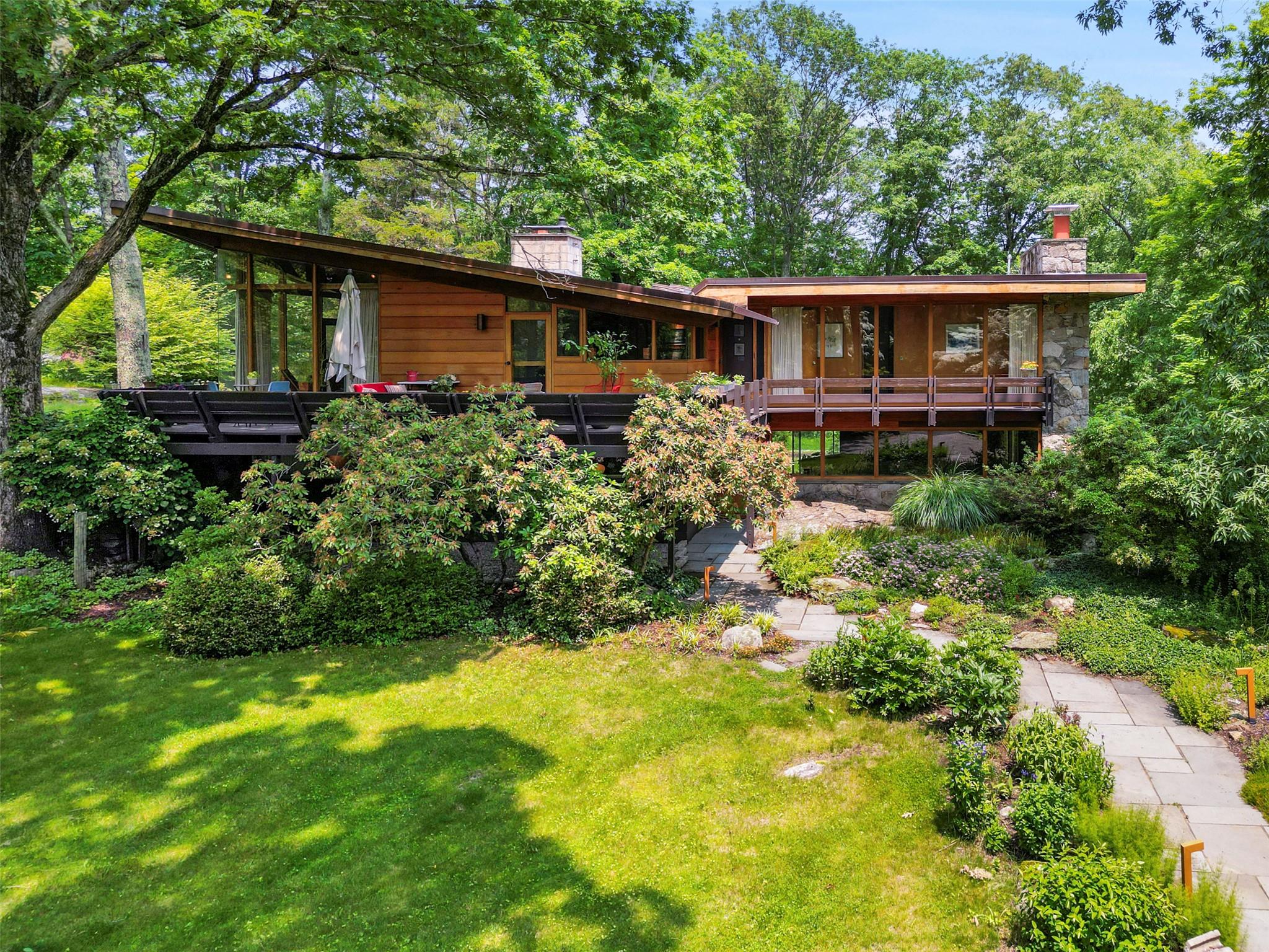 Quintessential Mid-Century Style. Classic Modern designed by David Henken, a disciple of Frank Lloyd Wright. Stunning interior spaces with a soothing, urbane aesthetic. Slate and wood floors, seamless mahogany paneling and ceilings and rare mitered glass windows. Beautifully scaled rooms with remarkable light and views. Phenomenal Great Room with vaulted ceiling and fireplace. Sleek Kitchen. Den with fireplace. Dramatic Family Room with fireplace incorporating river stones and a native rock outcropping. Private Primary Suite with Spa Bath. One additional Bedroom plus “Hotel” Guest Room crafted of Mahogany. Two additional Baths with high-end fittings. Perfectly nestled in a private setting overlooking gardens and woodlands. The perfect getaway complete with sparkling Swimming Pool.