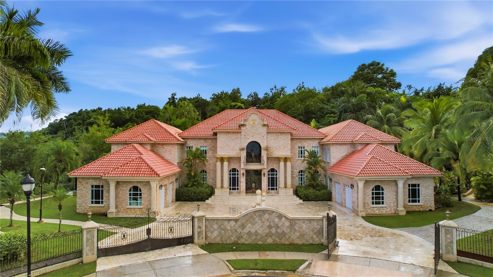 Classic Mediterranean-Style Mansion An imposing Mediterranean-style mansion, conceived under the highest standards of ultra-luxury and located in the exclusive Montehiedra community in San Juan. This residence satisfies the most discerning tastes, combining scale, privacy, and resort-style amenities while integrating the best of countryside and city living. With over 16,000 square feet of construction on nearly two acres, it offers a residential experience without precedent, designed for elevated daily living and large-scale entertaining.Interiors The layout is designed for absolute comfort. The property features five primary suites and thirteen bathrooms; all finished with premium materials. The master suite, spanning approximately 2,200 square feet, serves as a private retreat with its own kitchen, spa-style bathroom with steam shower and jacuzzi, and expansive walk-in closets. Social spaces are articulated with elegance: a double-height living room, a formal dining room for 16 guests, service bar, and both formal and informal salons for distinguished entertaining. The private cinema, with seating for 15, delivers a first-class audiovisual experience. All spaces are enriched with fine mahogany furnishings.Second Level Includes a sound area and a prayer room with full bath and terrace, convertible into an additional bedroom or multipurpose room.Third Level Conceived as a cultural and professional space, with capacity for up to 2,500 books—ideal for a private library, archive, or research study. It also includes an office/library and bathroom, reinforcing its representative character.Exteriors The exterior is a true recreational complex. Two heated saltwater pools—one of 30,000 gallons and another of 20,000—are complemented by jacuzzis, heaters, waterfalls, and slides reminiscent of an aquatic park. Pergolas, terraces, and landscaped areas with farm-style planting zones and fruit trees integrate leisure with domestic production. For wellness and activity, the property offers a 15 x 30 ft gym, dry and steam saunas, basketball and volleyball courts with bleachers for 100 spectators, plus playful features such as an equipped treehouse and dollhouse.Infrastructure & Security The residence includes four garages, an 8,000-gallon water tank, a 100 kW three-phase generator, a full-house sprinkler system, and anti-fungal treatment on all exterior stone. The exterior also offers more than 30,000 square feet of versatile pavement for events, parking, or recreational use, expanding possibilities for grand receptions or private gatherings.Privileged Location Just one minute from Expressway #52, with alternate access via Teodoro Moscoso and Avenida Baldorioty de Castro to Luis Muñoz Marín International Airport. The property is only 10 minutes from Puerto Rico’s Medical Center, steps from Montehiedra Mall Outlet, 15 minutes from Plaza Las Américas, and 25 minutes from The Mall of San Juan, home to ultra-luxury boutiques. Montehiedra is a respected enclave, with 24/7-armed surveillance and amenities including pools, tennis, pickleball, volleyball, and basketball courts, as well as a clubhouse.Unique OpportunityThis mansion represents a singular opportunity in Puerto Rico’s luxury market: a home conceived as a private sanctuary and the perfect stage for large-scale entertaining and distinguished representation.