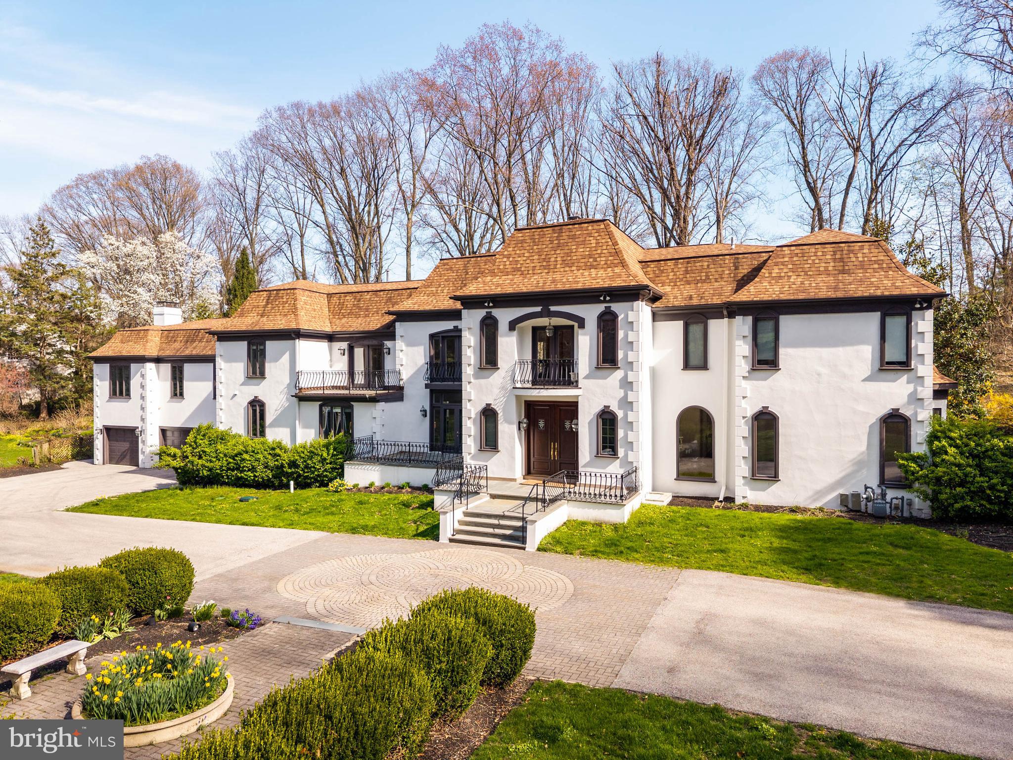 Positioned behind dual gated entrances on over 1.5 professionally landscaped acres, 1075 Green Valley Road is a French Colonial residence offering nearly 8,000 square feet of living space, extensively updated and meticulously maintained. A circular paver drive creates a strong sense of arrival, leading to double doors that open to a two-story foyer with herringbone hardwood floors and inlay, anchored by a sweeping turning staircase.The main living spaces are defined by scale, light, and direct access to the grounds. The living room features floor-to-ceiling windows and a wood-burning fireplace, while a sitting room and dining room sit opposite, each opening through French doors to slate patios. Across the main level, the principal rooms connect seamlessly to the outdoor terraces, creating a natural extension of the living space for both everyday use and entertaining.At the center of the home, a vaulted gathering space integrates a family room, game area, library, and office into a single, expansive environment. This space has been extensively remodeled with updated flooring, custom built-ins, a wet bar, and Murano glass chandeliers, along with modern enhancements including WiFi-controlled lighting and an integrated motorized TV lift. Direct access to the patios reinforces the connection to the surrounding grounds.The kitchen is both functional and inviting, with custom cabinetry, granite countertops and backsplash, stainless steel appliances, and a fireside dining area. Skylights and surrounding windows provide consistent natural light, while the adjacent enclosed porch with a built-in grill extends the space for year-round use.Upstairs, the primary suite includes a fireplace, a spacious bath with soaking tub, glass-enclosed shower, built-in vanities, and an oversized dressing room with custom built-ins. Additional bedrooms are well-proportioned with access to updated baths, including a spa-inspired bath featuring a wet room, freestanding tub, dual showers, and custom finishes.The fully finished lower level adds another layer of functionality, featuring additional living space, fitness area, full bath, and sauna—well-suited for guests, recreation, or private retreat.The outdoor setting is defined by multiple slate patios, mature landscaping, and a lagoon-style swimming pool with integrated spa, creating a resort-like environment.Extensive mechanical and infrastructure upgrades have been completed, including new heating and air conditioning systems, comprehensive insulation improvements, LED lighting throughout, WiFi-enabled thermostats, and a repaired septic system. Exterior improvements include full stucco remediation and painting, upgraded irrigation with WiFi control, enhanced gated entry systems with video and remote access, and new pool equipment.Located in Lower Merion Township with convenient access to Route 30 and I-76, and within close proximity to the Main Line’s schools, clubs, and dining, 1075 Green Valley Road offers a rare combination of scale, setting, and meaningful upgrades, aligned with the expectations of today’s buyer.