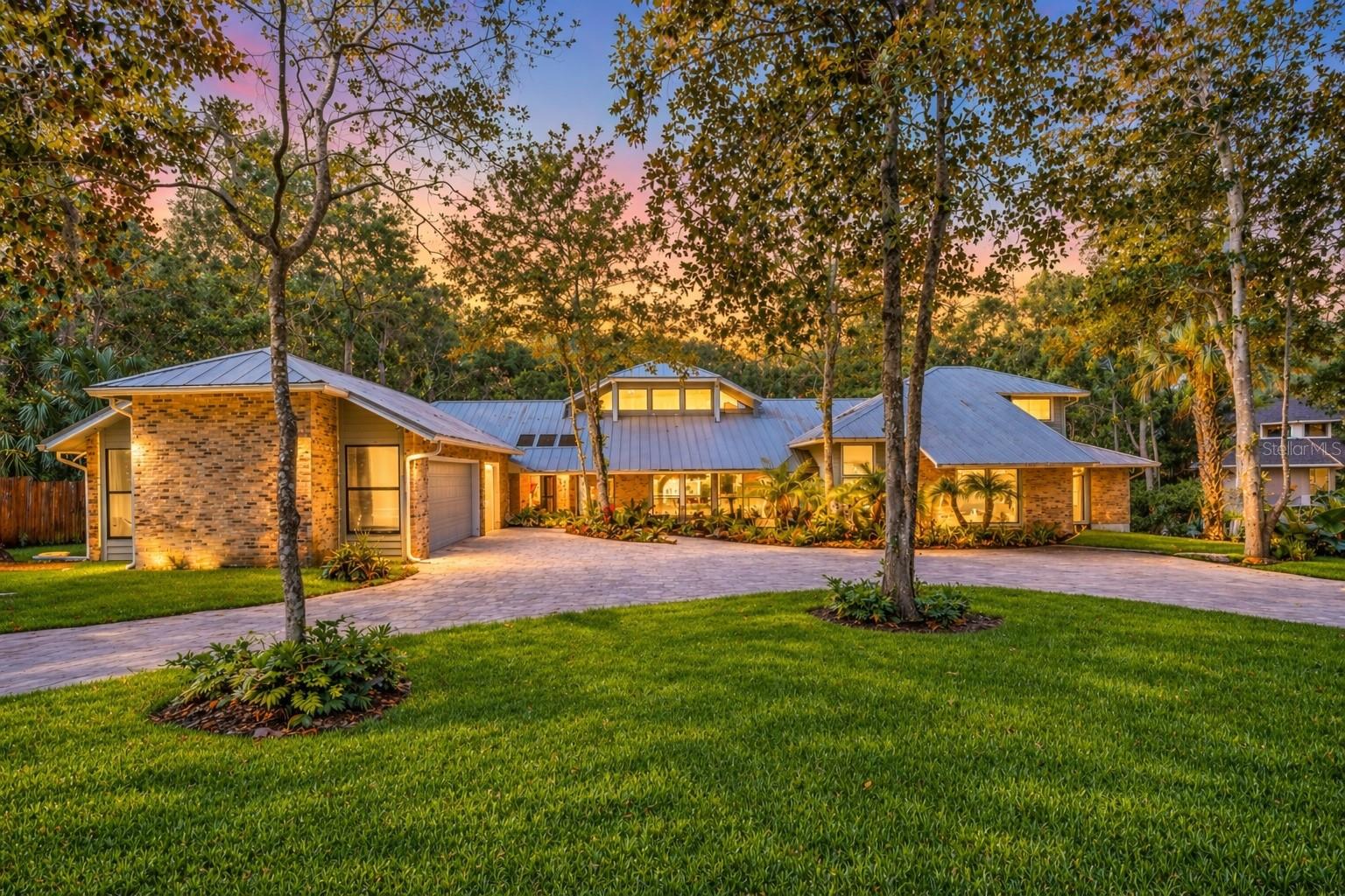 Welcome to 20 Twelve Oaks Trail, located at the end of a quiet cul-de-sac in The Trails. This stunning custom riverfront estate opens into a world of privacy, scale, and architectural presence that is almost impossible to replicate. Set on 1.31 wooded acres along the Tomoka River, the property feels hidden, calm, and deeply connected to its natural setting, with mature trees, a long circular drive, and a sense of arrival that begins before you ever step inside. The house itself is striking in a way that ordinary luxury homes are not. Designed with real architectural intention and modern finishes, it unfolds through soaring ceilings, expansive glass, strong lines, and light-filled spaces that pull the outdoors inward at every turn. The main living spaces are dramatic without feeling cold, open without losing intimacy, and unmistakably custom in character. No detail was overlooked in the recent renovations: ROOF (2023) • A/C (2023) • MOST WINDOWS & SLIDERS (2024) • BATHROOMS UPDATED (2024/2025) • NEW FLOORING IN BEDROOMS & FAMILY ROOM (2025) • REFRESHED LANDSCAPING, NEW LIGHTING & IRRIGATION (2025) • FRENCH DRAIN SYSTEM. The kitchen anchors the home’s central gathering spaces and flows naturally into the surrounding living and dining areas, creating a layout equally suited to quiet daily life and large-scale entertaining. Broad sightlines and oversized sliders connect the interior to a screened pool and spa environment that functions as a true extension of the house, making indoor-outdoor living feel effortless and complete. Beyond the pool, the property becomes something rarer still. An elevated walkway carries you through the trees to a private dock on the Tomoka River, where the setting opens into sky, water, and stillness. It is a sequence that gives the property its emotional center and makes the experience of being here feel more like a retreat than a residence. Morning coffee by the water, afternoons on the dock, evenings under the landscape lighting, and the quiet of the river just beyond the trees give this home a lifestyle few properties can genuinely offer. The floor plan is expansive and flexible, with generous spaces for guests, office use, hobbies, fitness, entertaining, or multigenerational living, all without sacrificing cohesion. The primary suite is spacious and private, and the additional living areas offer unusual versatility while preserving the strong architectural through-line that makes the home feel unified and intentional.Private yet convenient, the property is just minutes from Granada, I-95, and the beach, while feeling entirely removed from the pace of everyday life. This is not a typical listing and should not be approached as one. It is a custom riverfront compound for a buyer who values privacy, beauty, architectural character, and the rare feeling of having arrived somewhere that is truly special.