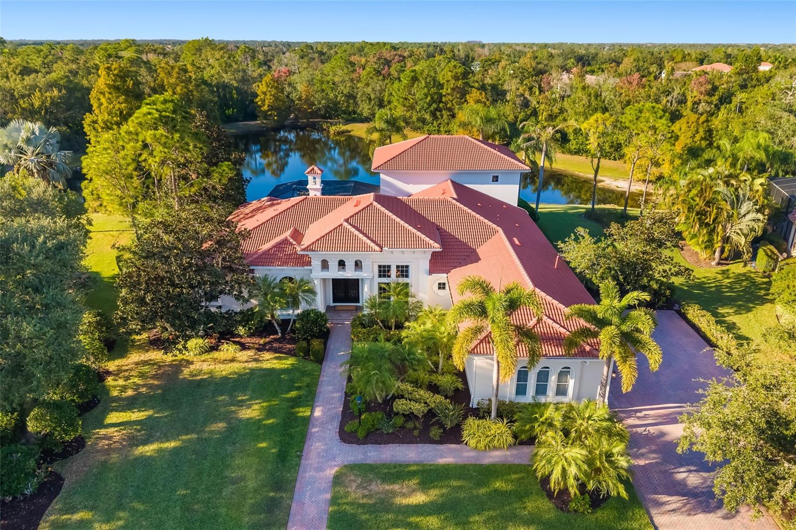 A rare sanctuary of architectural grace and unrivaled privacy in one of the most prestigious enclaves of Lakewood Ranch Country Club. Offered turnkey furnished, this distinguished two-story estate is positioned on over a half-acre with unobstructed views of the lake and protected preserve with no neighboring homes in sight. The grand herringbone-patterned paver walkway and extended driveway with a side-entry three-car garage set a tone of timeless sophistication. Hurricane-rated fiberglass double entry doors, crafted to emulate wrought iron, open to more than 4,800 square feet of refined living space adorned with travertine flooring, Corinthian columns and sweeping water views. Four separate bedroom suites with walk-in closets, a dedicated office, living room fireplace, 14-foot dining ceilings and a family room. A large flex room offers versatility for a theater, gym, or game retreat, while the laundry room's window fills the large workspace with natural light. Abundant storage.  Upstairs, a bonus room with wet bar and private guest suite capture panoramic views of the lake, woods and abundant wildlife. Outdoors, the pool, spa, outdoor kitchen and shower offer total seclusion, completing this exceptional home where timeless architecture facilitates complete tranquility.