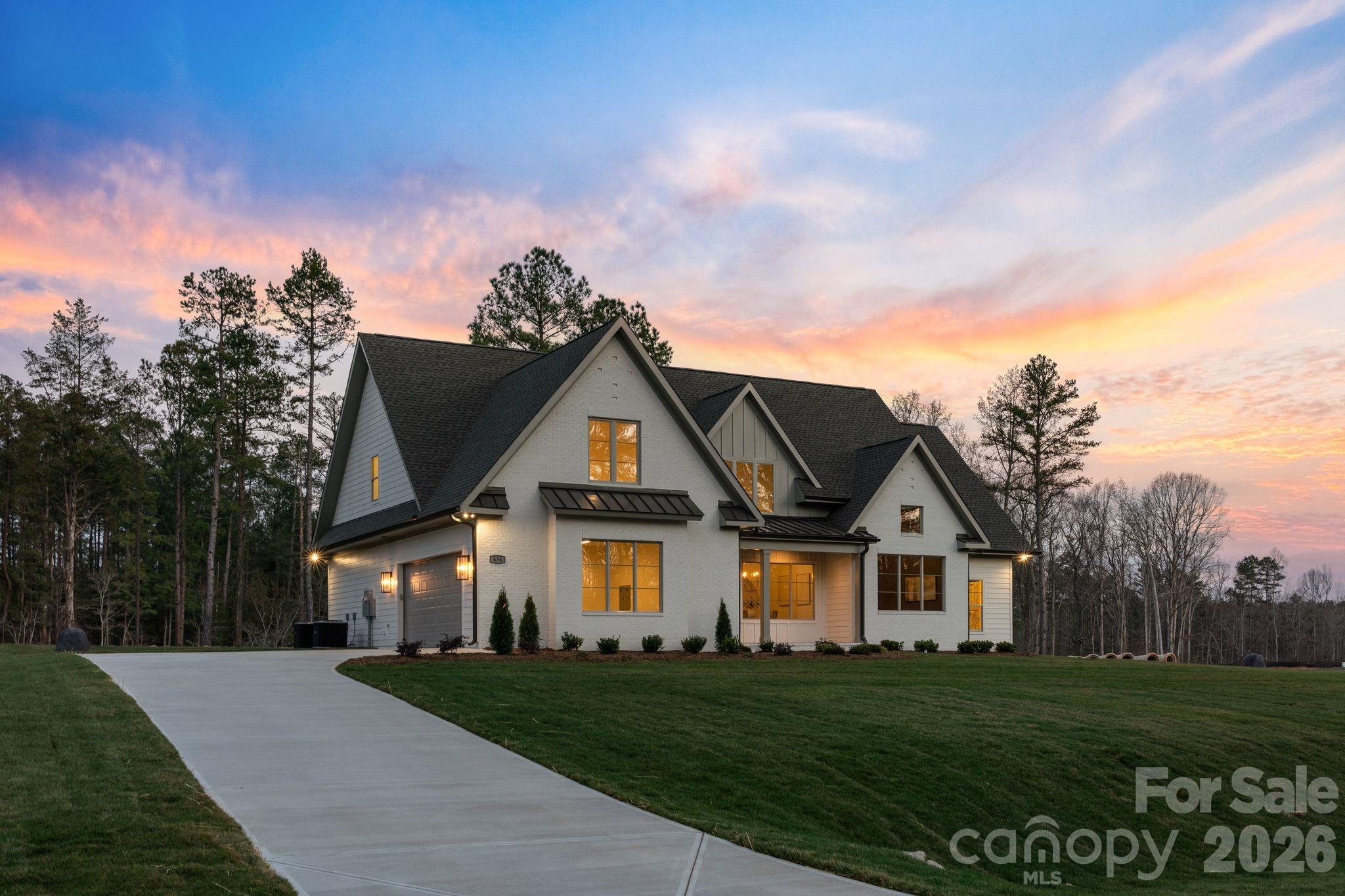 Nestled within an intimate 36-homesite community where every residence sits on over an acre of land, this exceptional home represents a level of craftsmanship and architectural detail rarely found in the Clover market. Perfectly positioned along the community pond, the property enjoys peaceful water views and a setting that blends privacy, space, and natural beauty.From the moment you arrive, the striking exterior architecture and beautifully manicured grounds set the tone for what lies inside. Full sod and irrigation frame the home, while the thoughtfully designed layout and placement on the homesite create an inviting sense of openness and tranquility.Step inside and immediately appreciate the refined design and attention to detail. Elegant architectural arches create graceful transitions throughout the home, adding a level of character and sophistication rarely seen in newer construction. The open floor plan allows natural light to fill the main living spaces, while a carefully curated lighting package enhances the warm and welcoming atmosphere.At the heart of the home is a stunning chef’s kitchen that balances beauty and functionality. Extensive custom cabinetry, a statement vent hood, marble countertops, farmhouse sink, and high-end appliances create a space designed for both entertaining and everyday living. The kitchen flows seamlessly into the spacious living area, where a sleek fireplace and thoughtfully designed built-ins create the perfect setting for gathering with family and friends.The primary suite offers a peaceful retreat, featuring a beautifully designed bath complete with a large walk-in shower, freestanding soaking tub, and custom cabinetry that blends elegance with everyday comfort.Upstairs, additional bedrooms and well-appointed bathrooms provide comfortable accommodations for family and guests, while a spacious upper-level bonus area offers flexibility for a media room, playroom, home office, or secondary living space.Outdoor living is equally inviting. The covered rear patio overlooks the community pond, creating a serene backdrop for morning coffee, evening relaxation, or entertaining while enjoying the quiet natural surroundings.Located just minutes from dining, shopping, coffee shops, and everyday conveniences — and only a short drive to Charlotte Douglas International Airport — this remarkable property offers the rare opportunity to enjoy space, privacy, and luxury living in one of Clover’s most distinctive communities.This is more than a home — it is a showcase of quality, thoughtful design, and timeless craftsmanship.