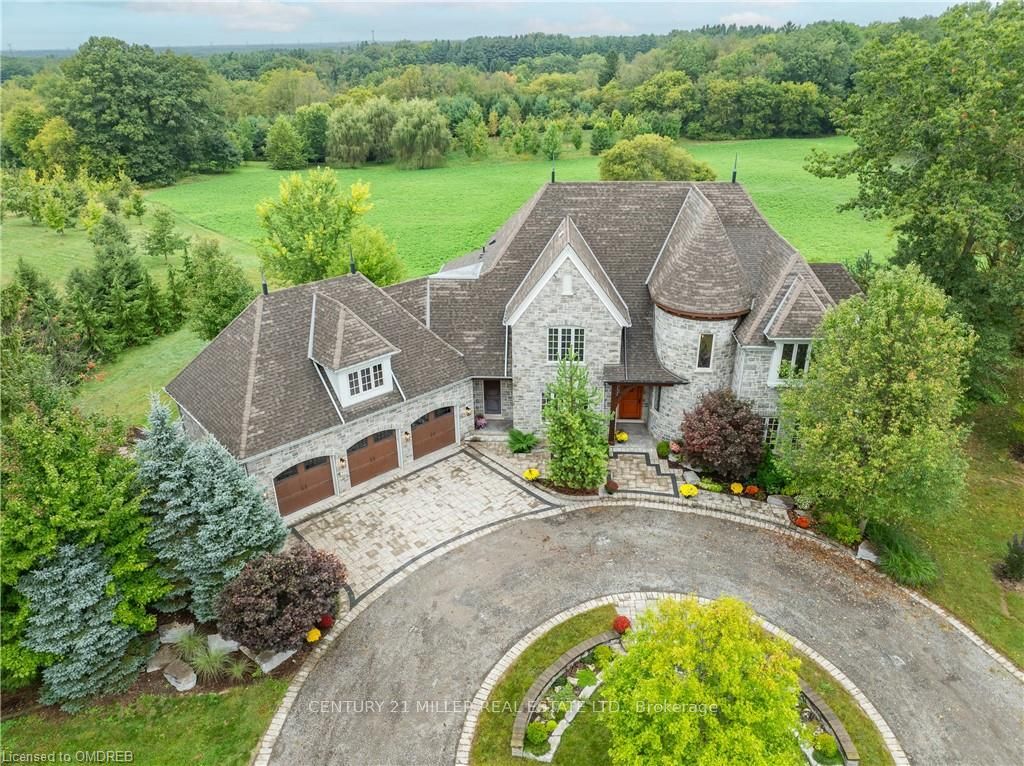 Nestled on 25 acres of rolling hills and serene forest, this stunning executive estate offers 4850 square feet of luxury living. Add another 2800 square feet of unfinished basement and this home will exceed your expectations. A large great room boasts a stunning 23-foot beamed ceiling and a floor-to-ceiling stone gas fireplace. A cozy main floor office, complete with gas fireplace, provides the ideal spot for remote work or quiet reflection. The gourmet kitchen features a walk-in pantry, top-tier appliances and an eat-in area with access to the outdoor porch. A butler's pantry adds convenience for entertaining or serves as a charming morning coffee bar. Wide plank hand-scaped hickory floors create a warm ambiance, while 8-foot solid oak doors elevate the luxurious feel of every room. A striking winding staircase connects all levels of this beautiful home. Upstairs offers a large primary bedroom with 5-piece ensuite and walk-in closets. Three additional large bedrooms provide ample space for family and guests. For added convenience, a fifth bedroom on the main floor offers the perfect space for a nanny or in-law suite. Minutes from the charming town of Ancaster, this estate provides easy access to shopping, dining and local amenities while maintaining the serenity of rural living. Experience the perfect blend of luxury and nature in this exceptional estate. Schedule your private showing today.