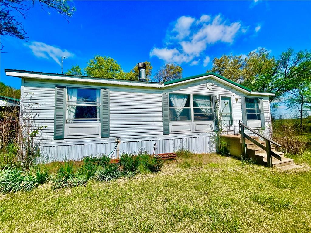 Hobby Farm Time! 3/2 Manufactured home in wonderful shape on almost 3 acres of lush Missouri acreage. Tons of specialty trees, flowering bushes and perennials to work with. Massive Garden & orchard potential. Big rooms & an open, comfortable  floor plan. REAL WOOD burning fireplace in the living room, Newer roof. Private well and septic. Existing ramp on the back entrance if needed for handicapped. Newer Custom carport attached to concrete for additional deep protection, storage, or use for a covered outdoor patio and fun summer kitchen. Efficient propane heat furnace and AC work well throughout the summer and winter seasons. Tons of potential to make this property your own. Its a deal!