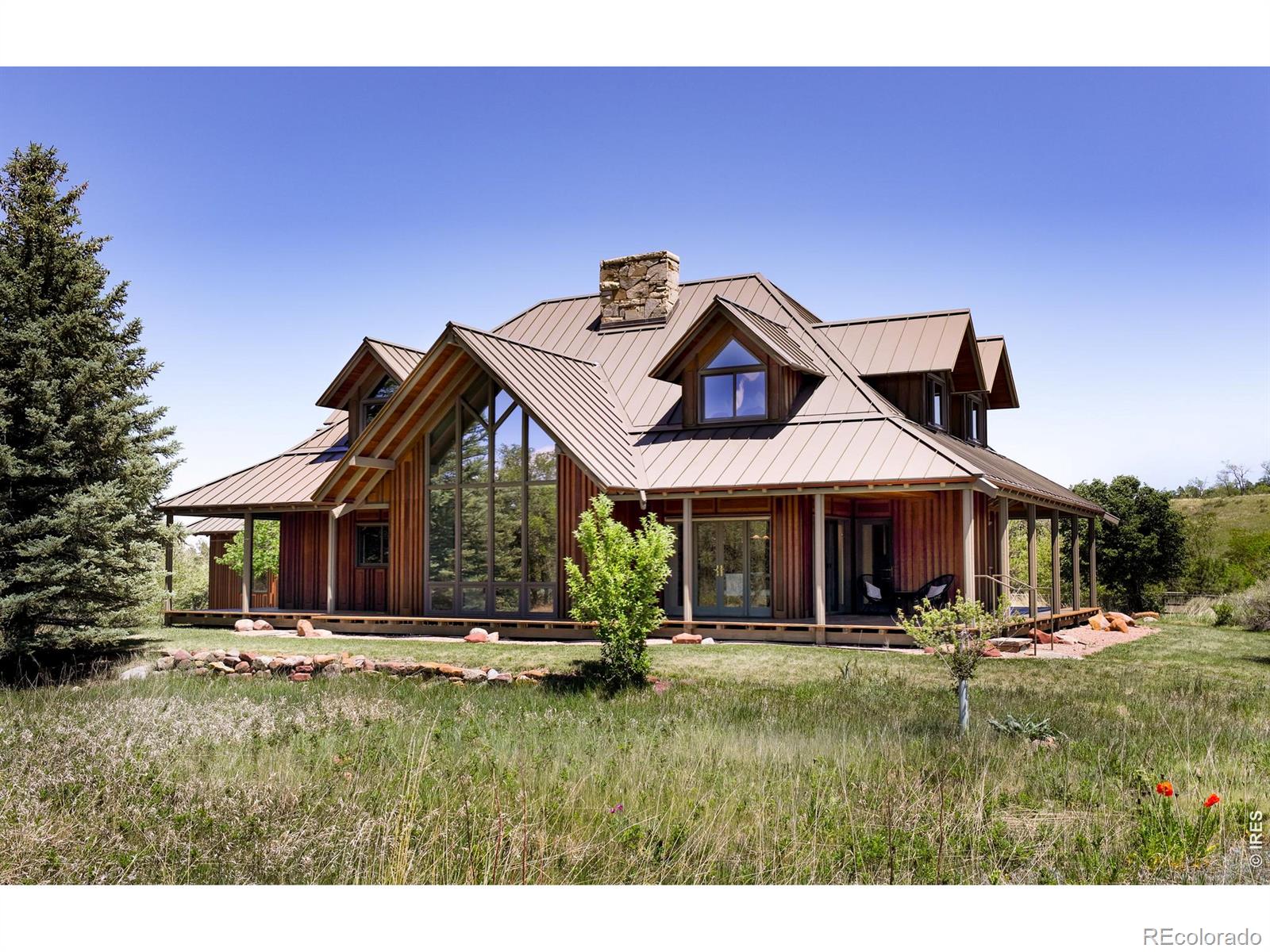 Tranquil country living meets impressive architecture in this midcentury 4BD/3BA by revered architect Hobart D. Wagener. Add your personal touches to reimagine this notable home. This exceptional 3.5-acre property delivers awe-inspiring mountain views, a three-stall barn, and a three-car heated garage topped by a studio - all just 10 minutes from S. Boulder. Built in 1993 for Wagener's son and his family, the 2,820 SF home embraces the architect's hallmarks, including wood paneling and a distinctive metal roof. Massive windows and natural materials bring the outdoors inside and put mesmerizing views center stage. A covered wraparound porch invites you inside, where ceilings soar above wood floors, stone walls, and custom woodwork by Harv Mastalir - a local master artisan. The entry flows to a vaulted living room flanked by a wood-burning stove and a wall of windows framing postcard outlooks. The corner dining room offers extra-wide glass doors. Every room on the main level offers porch access for seamless indoor-outdoor living. The large kitchen includes cabinetry, a center island, and an adjacent laundry room. A spacious family room with custom built-ins and a guest suite complete the main floor. The dramatic cantilevered staircase leads to a vaulted owner's suite with three closets and a windowed bathroom, while two secondary bedrooms share a split bath. A long gravel drive meanders past split-rail fencing, grassy pastures, mature trees and a vegetable garden, creating 240 feet of separation from the nearest road. The heated 2003 garage is equipped with generous storage, a wine cooler, a sink and solar panels. Above, the large studio is perfect for a guest, art or fitness space. A 2005 barn with a corral makes this the ideal equestrian property. Fresh paint, new UV-filtered well water, water heater and septic system. Minutes from world-class trails, Eldorado Springs Pool & Ballroom, Eldorado Canyon State Park, plus S Boulder, Table Mesa and Superior amenities.