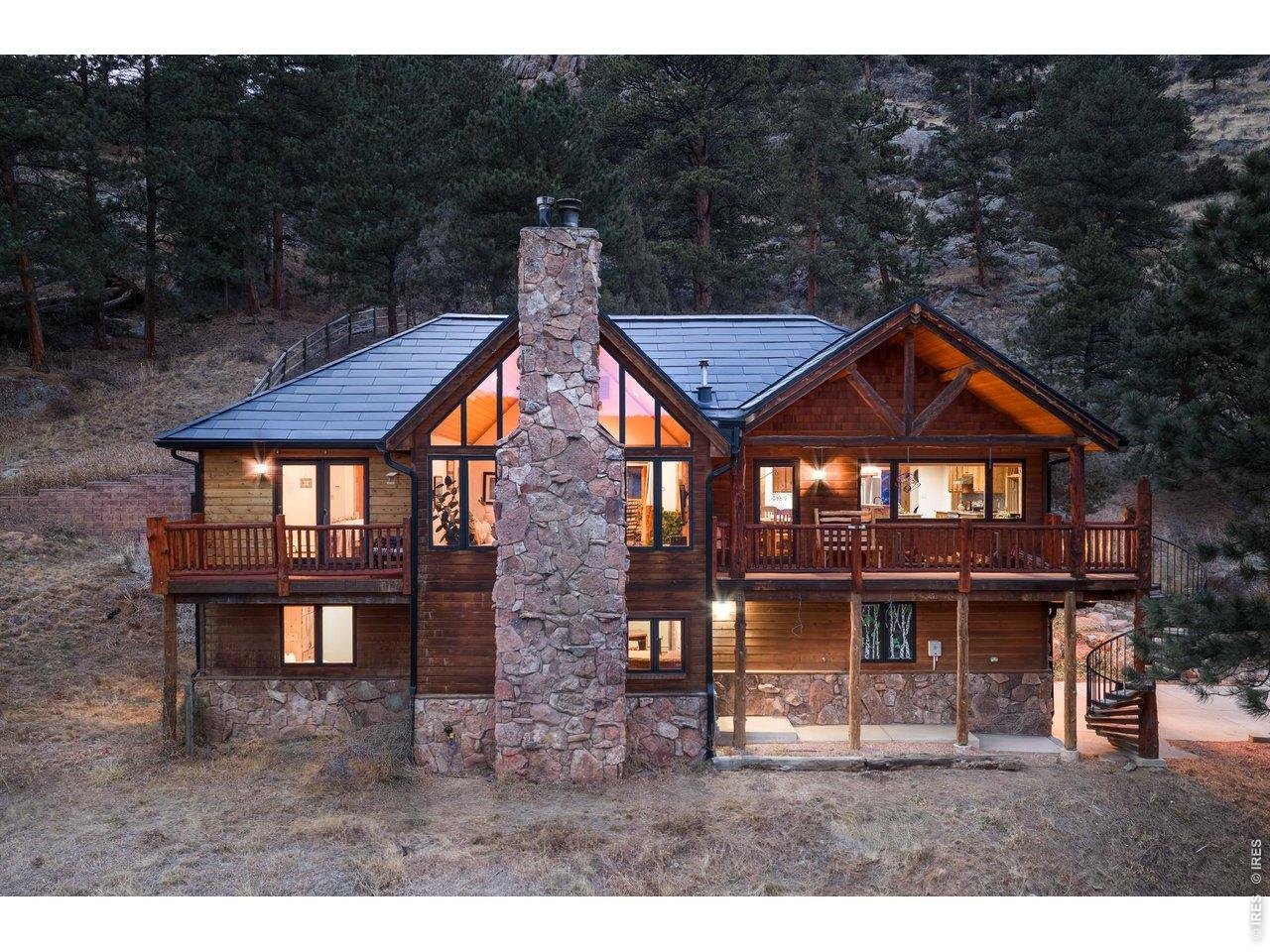 One-of-a-kind environmentally conscious mountain home on 1.47 acres backing to National Forest with panoramic south-facing views from nearly every window and deck. Soaring ceilings, dramatic south-facing windows, and a massive moss rock fireplace define the great room. Artisan finishes throughout including hand-peeled log accents, native flagstone, slate, and recently refinished hardwood floors. Primary suite features fireplace, private deck, tiled bath, and dual walk-in closets. Updated kitchen with new granite countertops and custom cabinetry. One of the home's most distinctive features is the tavern-style bar with log siding, historical red brick and sandstone accents, an unforgettable space for your next gathering. A unique indoor atrium/rainforest office brings nature inside year-round, while the enclosed sunroom adds over 220 square feet of additional flexible living space beyond the home's core interior space. Oversized decks, terraced garden space, custom stone walkway, new custom metal railing, and concrete driveway - a luxury in the mountains. Rare (owned) Tesla solar roof tiles are beautiful and so much better than solar panels. Enjoy low electric bills thanks to the solar roof! Updated mechanical systems including boiler, water heater, and whole house water filtration system + under sink filter. Cistern / reclamation tank for watering plants or garden, Direct access to hiking trails from your backyard. A truly distinctive mountain retreat minutes to downtown Lyons and only 20 minutes to Rocky Mountain National Park.