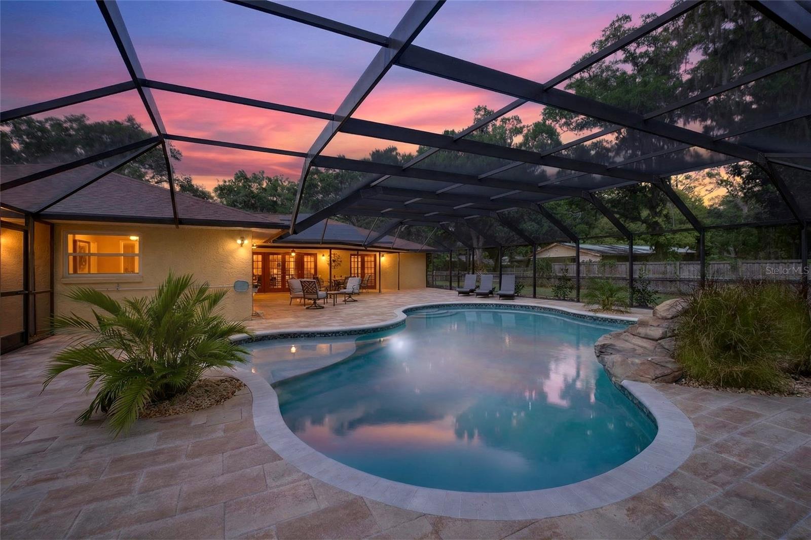 *Multiple Offers Received* A rare blend of timeless character and multi-generational flexibility—this extraordinary Lutz estate offers space, privacy, and craftsmanship in a grand yet personal setting. Set on 1.2 acres of open, park-like grounds, the property unfolds behind a charming picket fence. A sprawling paver patio and walkway lead to a wood double-door entry. Inside, the home immediately captivates with a sunken living room featuring dramatic wood plank ceilings with exposed beams, skylights that fill the space with natural light, and elegant French doors that open seamlessly to the screened lanai and pool—your private outdoor oasis designed for relaxation and entertaining. Throughout the 2630 sq ft main residence, architectural details abound, including high baseboards, smooth ceilings, porcelain tile and engineered hardwood floors, crown molding, and recessed lighting—all contributing to a warm, inviting aesthetic. Major updates include a roof(2020), A/C(2022, serviced 2026), water heater(2025), and solar panels (2022). Average electric bill is $200/month powering both homes and the pool. Seller will pay off the solar panels at closing. The formal dining room offers a refined setting with chair rail and plantation shutters. A full bathroom off the foyer provides convenience for guests and direct access to a secondary bedroom. The spacious kitchen is both functional and beautifully designed, featuring tall raised-panel wood cabinetry with crown molding, granite countertops, a full tile backsplash, and stainless appliances(2024–2026). A peninsula breakfast bar and built-in pantry with pull-out shelving add convenience. Just off the kitchen, a generous dining area is filled with natural light from skylights and features French doors that open to the pool area. The inviting living space centers around a wood-burning fireplace framed by brick extending to the ceiling, anchored by a matching hearth with elongated windows on either side that enhance the room’s warmth and character. Multiple sets of French doors lead to the lanai, creating a seamless indoor-outdoor flow ideal for entertaining. The primary suite offers a private retreat with shiplap accents, both a standard and walk-in closet, and French doors leading to the lanai. The ensuite bath features dual sinks, granite countertops, and a tiled walk-in shower. Additional generously sized bedrooms provide flexible space for family, guests, or home office. Beyond the main home, a fully equipped 936 sq ft detached guest house offers incredible flexibility—ideal for in-laws or extended stays. With its own private entrance, full kitchen, dining area, laundry, and spacious bedroom suite, it truly lives like a home within a home. Step outside to your private oasis, where a heated 24,000-gallon saltwater pool(2024) takes center stage. Designed with a freeform shape, the pool features a rock formation waterfall, an in-water sun shelf with bubblers, and a 7-foot-deep end, all surrounded by a paver deck. The covered lanai and fully screen-enclosed pool area provide year-round comfort and enjoyment. The expansive grounds continue with a detached third-car garage with a workshop area, and ample space to enjoy the tranquility of this unique setting—perfect for RVs. This private estate offers serene living just minutes from major highways, dining, shopping, and convenient access to Tampa International Airport and downtown. This is more than a home—it’s a rare lifestyle opportunity.