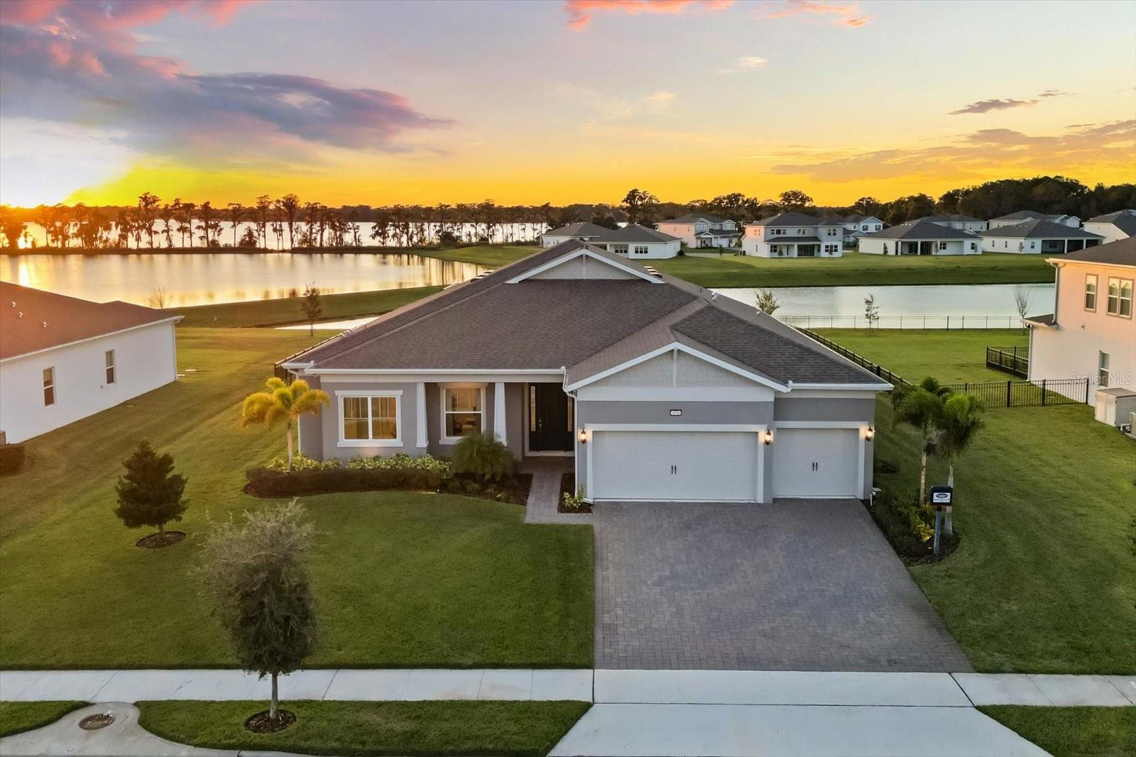 Built in 2023, this single-story home in the gated community of Sunset Preserve blends modern design, refined finishes, and effortless Florida living. The open-concept layout features eleven-foot ceilings, wide-plank luxury vinyl floors, and decorative accents that enhance the sense of space. Expansive sliding doors fill the home with natural light and open to a tranquil outdoor retreat overlooking a peaceful pond with Lake Pickett just beyond.
The gourmet kitchen is the heart of the home with upgraded KitchenAid appliances, an oversized island, quartz countertops, and soft-close cabinetry. The layout flows seamlessly into the spacious living and dining areas, creating the perfect setting for gatherings and everyday comfort. The primary suite offers a true escape with dual walk-in closets, a spa-style bathroom with a soaking tub and frameless glass shower, and private views of the water.
Three additional bedrooms, including a Jack and Jill suite, are thoughtfully positioned for privacy, while a front office adds flexibility as a fifth bedroom or creative workspace. The extended three-car garage provides abundant storage, complemented by energy-efficient construction and premium finishes throughout.
Step outside to a screened lanai with a resort-style pool and spillover spa, where you can relax and watch the sunset reflect across the water. Sunset Preserve residents enjoy private access to Lake Pickett with a community boat ramp, dock, lakefront pavilion, and playground. Conveniently located near 417, 408, and top-rated schools, this home offers the perfect balance of serenity, sophistication, and accessibility.