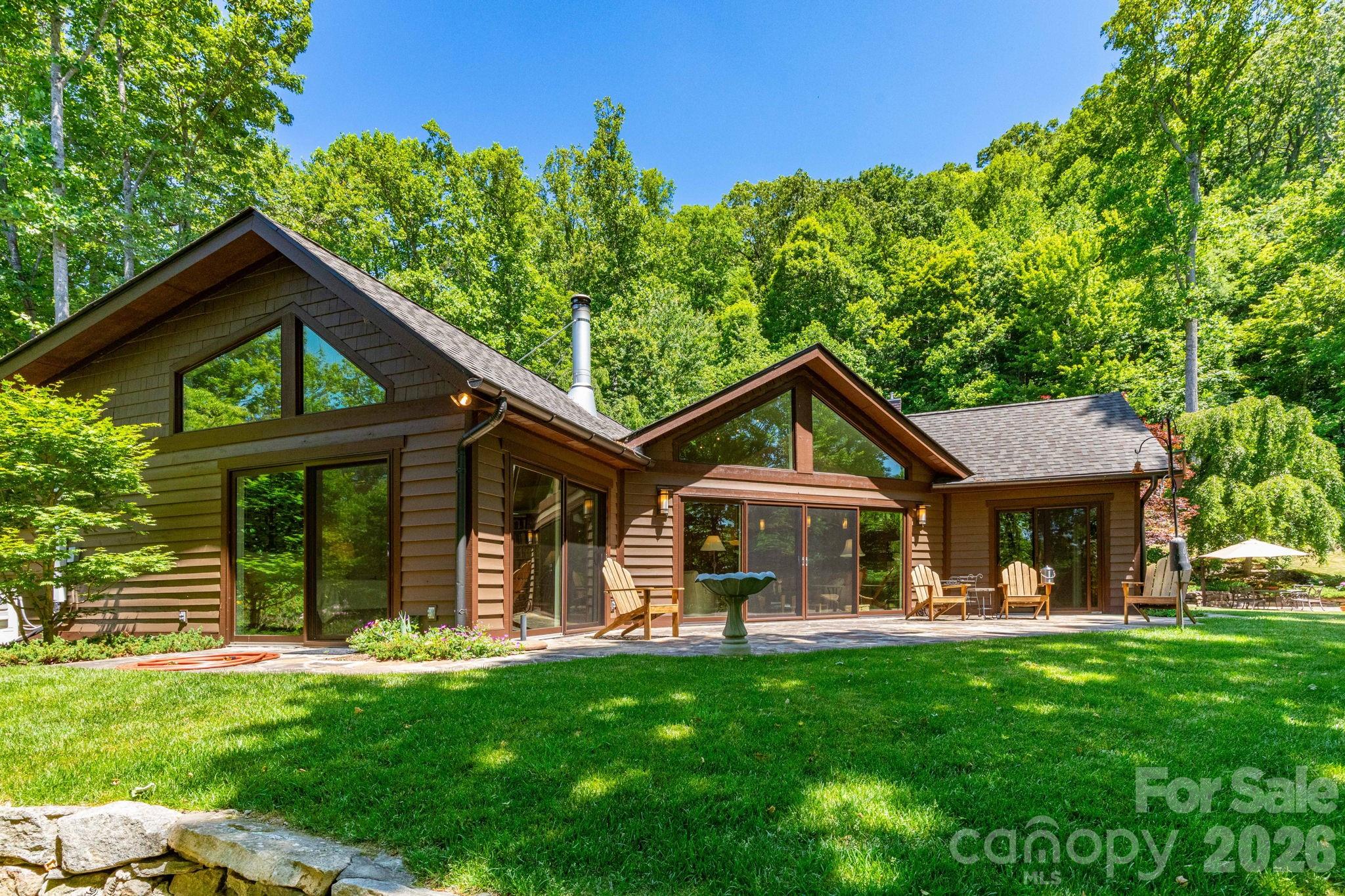 Experience a true mountain sanctuary unlike anything else on the market. Set on 3.24 acres—and paired with an additional 6.40-acre buildable parcel—this exceptional estate features two remarkable homes surrounded by curated gardens, mature trees, and peaceful natural elements. The current owners have been genuine stewards of the land, enhancing its beauty while preserving its integrity. The property offers a tranquil, park-like setting with perennial gardens, flowering bushes, stone meditation paths, and multiple private outdoor patios. Enjoy six months of cooling shade under the trees and six months of long-range winter views. Extensive stone retaining walls, a commercial-grade rainwater management system, and a private stream with a waterfall and spring-fed sitting pool create an atmosphere of pure serenity. The main residence rises naturally from the landscape with floor-to-ceiling windows that welcome abundant natural light and capture seasonal mountain views. Inside, custom renovations throughout the kitchen, bathrooms, living room, and entryway deliver an open, airy feel with seamless indoor-outdoor flow. Radiant floor heating, mini-splits for year-round comfort, ceiling fans, a Lennox heat-circulating stone fireplace, and passive solar benefits add efficiency and warmth. Additional features include a new roof, a spacious laundry/pantry, a two-car garage with storage, a whole-house generator with an in-ground propane tank, and a water filtration system. The three-season screened porch with Easy Breeze windows extends the living space into nature, inviting moments of quiet and reflection. Follow garden paths to the second residence—an architect-designed Craftsman-style home blending artistry and rustic charm. Oak cabinets and flooring, beautiful windows, wainscotting, and timber-beamed ceilings milled from tulip poplar harvested directly from the property highlight its craftsmanship. A bright office/studio, a wide stone terrace, a small efficient kitchen, built-in bookcases, four bunk beds, a heat pump, ceiling fans, and a basement area with storage and a wine closet enhance its livability. An indoor sauna adds a retreat-like touch. Together, these homes and the surrounding land form a rare mountain haven—private, peaceful, and thoughtfully designed for those who value nature, intention, and timeless craftsmanship. With a deed restriction prohibiting short-term rentals, this property is meant to be truly lived in and cherished.