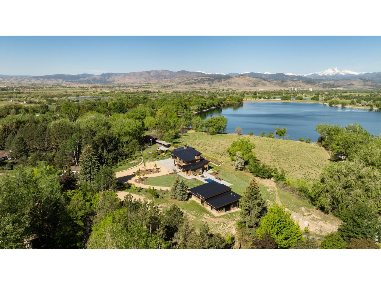 Lakeside living near Boulder is virtually unheard of, making 12357 N 75th Street one of the most exceptional opportunities in the region. Set on 7 lush, irrigated, acres with direct access to a private lake and sweeping views of Longs Peak, this Boulder County estate offers natural beauty, luxury, and privacy just 20 minutes from downtown Boulder. At the heart of the property is a newly constructed residence, thoughtfully designed for elevated indoor-outdoor living. Expansive accordion glass doors capture breathtaking views, bringing the landscape into every room. The kitchen is a standout, equipped with Sub-Zero and Wolf appliances, a steam oven, a striking steel range hood, wine storage, and a fully appointed butler's pantry. A dramatic open-hearth fireplace anchors the double height great room. Handcrafted cabinetry, reclaimed wood beams, and custom steel elements, create depth and sophistication. The home features four spacious bedrooms and six bathrooms, including a luxurious primary suite with a private loft, balcony, coffee bar, double-sided steel fireplace, spa bath with a soaking tub and steam shower, and a custom-designed walk-in closet. A dining room, private home office, and generous laundry room round out the home's well-appointed interior. Step outside to a true lifestyle haven. A heated pool and spa, lakeside fire pit, and expansive patios offer multiple venues for entertaining or unwinding in total privacy. Direct lake access provides the rare ability to paddle board, canoe, fish, or enjoy peaceful moments beside the water. The estate also includes a newly constructed agricultural barn, an original carriage house, and a freestanding art studio. Just down the road, the charming enclave of Hygiene offers a taste of small-town life, boutique shops, and community feel.