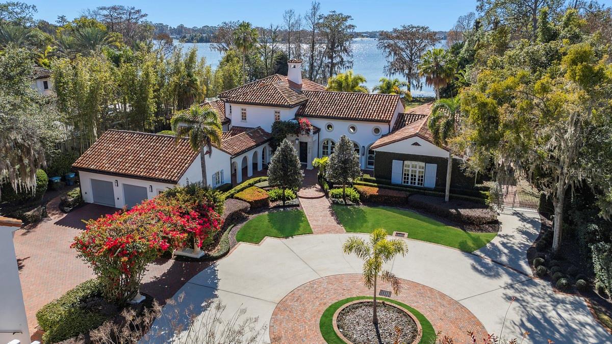 Villa Serenata — A Lakefront Legacy on Lake Maitland.Behind private iron gates along the storied shores of Lake Maitland, Villa Serenata presents a rare opportunity to own a distinguished Mediterranean estate on the renowned Winter Park Chain of Lakes. Set on approximately two acres of meticulously curated grounds, this extraordinary residence feels less like a home and more like a private resort—crafted for those who appreciate timeless architecture, thoughtful design, and elevated lakefront living.A sweeping circular driveway welcomes you beneath a canopy of soaring royal palms and majestic live oaks, immediately setting the tone for what lies beyond. As the automated gate opens, the property reveals itself as a serene sanctuary where elegance and privacy coexist in perfect harmony.The 6,634-square-foot main residence showcases interiors by acclaimed designer Ted Maines, unfolding across two levels of refined sophistication. The Mizner-inspired living room commands attention with dramatic 24-foot wood-beamed ceilings and twin walls of arched French doors—one framing sweeping views of Lake Maitland’s shimmering waters, the other opening to a sun-dappled courtyard where mornings naturally begin with coffee and quiet reflection.The upper level is devoted entirely to the primary suite, creating a private retreat complete with a heatless gas fireplace, spa-caliber bath with soaking tub and steam shower, a bespoke dressing room with custom built-ins, and a rooftop terrace with glass railings offering remarkable lake views. Three additional bedroom suites, each with an en-suite bath and generous walk-in closet, provide comfort and privacy for family and guests alike.At the heart of the home, the chef’s kitchen is equipped with Sub-Zero and Wolf appliances, custom cabinetry, and an expansive prep island designed to transition seamlessly from intimate family meals to catered gatherings of fifty. The formal dining room features a dramatic curved wall of windows, turning every meal into a lakefront experience, while the richly paneled library and office offer a quiet space for focused work or relaxed reading.Complementing the main residence is a thoughtfully designed guest compound totaling 1,540 square feet. A private media pavilion delivers a state-of-the-art theater and listening room for film enthusiasts and audiophiles, while the one-bedroom guest apartment above provides a fully appointed living space with kitchen, living area, and private entry—ideal for extended family, visiting guests, or live-in staff.Outdoor living is equally exceptional. Resort-style travertine surrounds the pool amid lush tropical landscaping, creating a tranquil setting for sun-filled afternoons. A covered lanai with full summer kitchen flows effortlessly from the family room, while an expansive open-air terrace extends from the great room—an inviting backdrop for sunset cocktails overlooking the lake.Villa Serenata is more than a residence—it is a legacy estate, offering privacy, architectural distinction, and a lifestyle centered on one of Winter Park’s most treasured waterfront settings.