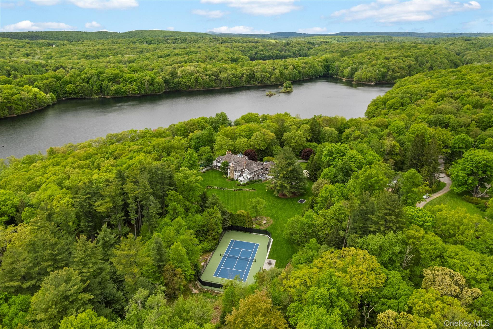 Discover your ultimate hideaway: a private, gated custom rebuilt 10,000 square foot Colonial nestled on over five majestic acres in Pound Ridge. While the impressive amenities are abundant, it is the serene setting that will truly capture your attention and your heart. Tucked behind a mature landscape, the property offers a retreat filled with quiet, tranquil spots. The grounds are thoughtfully designed for both relaxation and recreation, featuring a pool set off the side of the house and a secluded tennis court in the back. Inside, light floods the glass sunroom off the kitchen, and private decks extend from multiple rooms, including the luxurious primary suite. The heart of the home is the family room, boasting a dramatic, soaring ceiling height and anchored by one of three cozy wood-burning fireplaces. Welcome home!