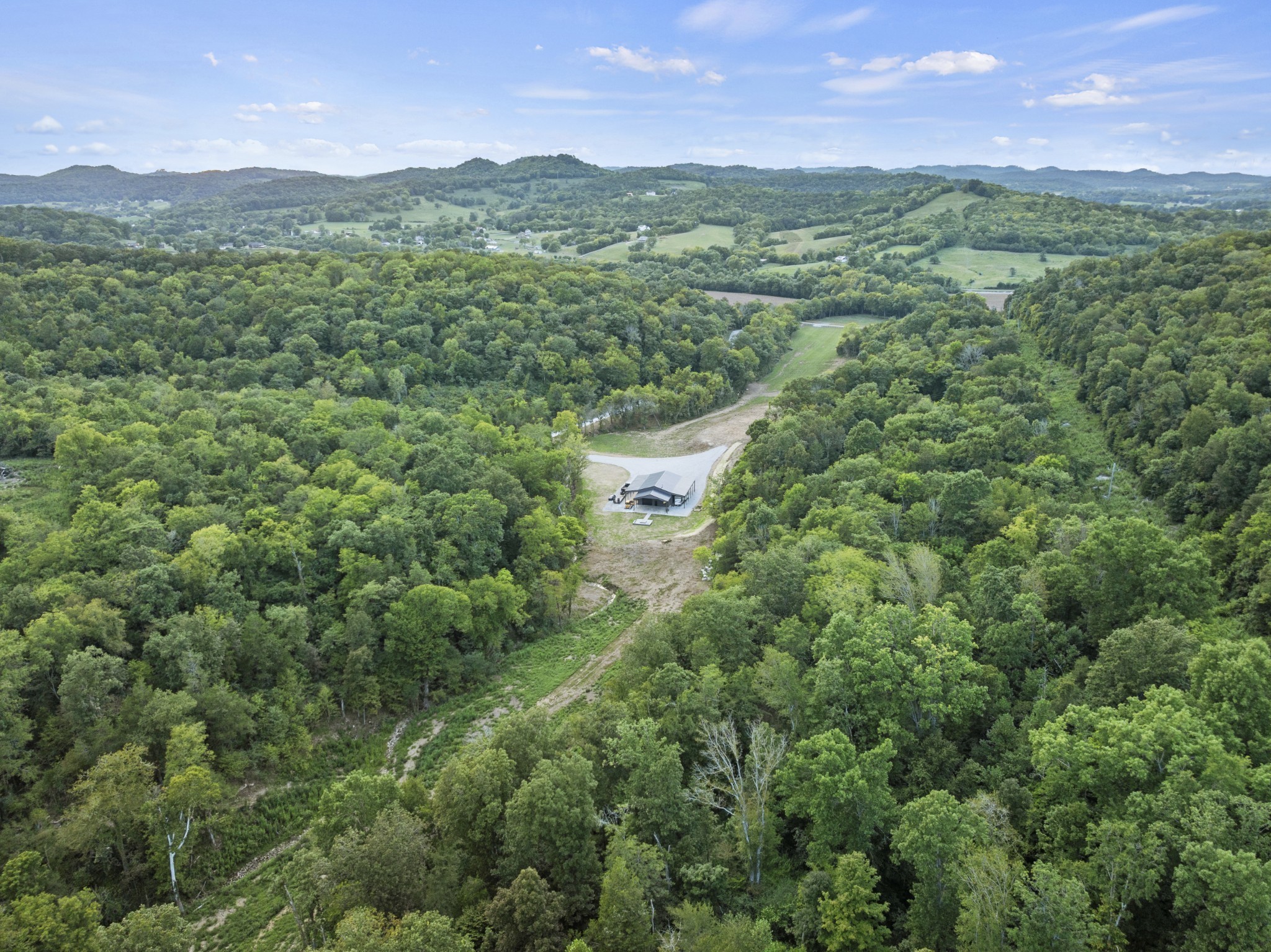 Enter this stunning 306.95 acre farm with black ranch fencing and a gated entrance, setting the tone for the privacy and beauty that awaits.The owner has thoughtfully completed the major groundwork—site excavation, driveway, utilities, and septic approval—so you can move straight into building your dream home and farm.   4-bedroom septic permit w/ electric & water already in place at the build site.  A 60x40 shop enhanced by lean-tos on each side, providing additional covered storage and workspace. Shop features a full bath, foam insulation, wood-plank interior walls, interior RV sewer, water & electric connection, wood burning stove and additional exterior RV hookup under the lean to for group camping adventures. Enjoy a custom hardscape patio complete w/outdoor kitchen and fire pit, perfect for entertaining.  The hillside behind the shop provides a natural backdrop for private long-range shooting. Located within 4 miles of I-40, offers over 1,200 feet of road frontage in a peaceful rural setting. The land includes rolling wooded hills, approximately 40 acres of pasture, multiple scenic building sites with breathtaking views and no visible neighbors as far as the eye can see, miles of atv/horse riding trails, natural springs, an old homestead, a newly dug pond, & peaceful creek that flows into Hickman Creek  Exceptional wildlife habitat with abundant deer & turkey, known locally for high-quality hunting. Fiber internet available