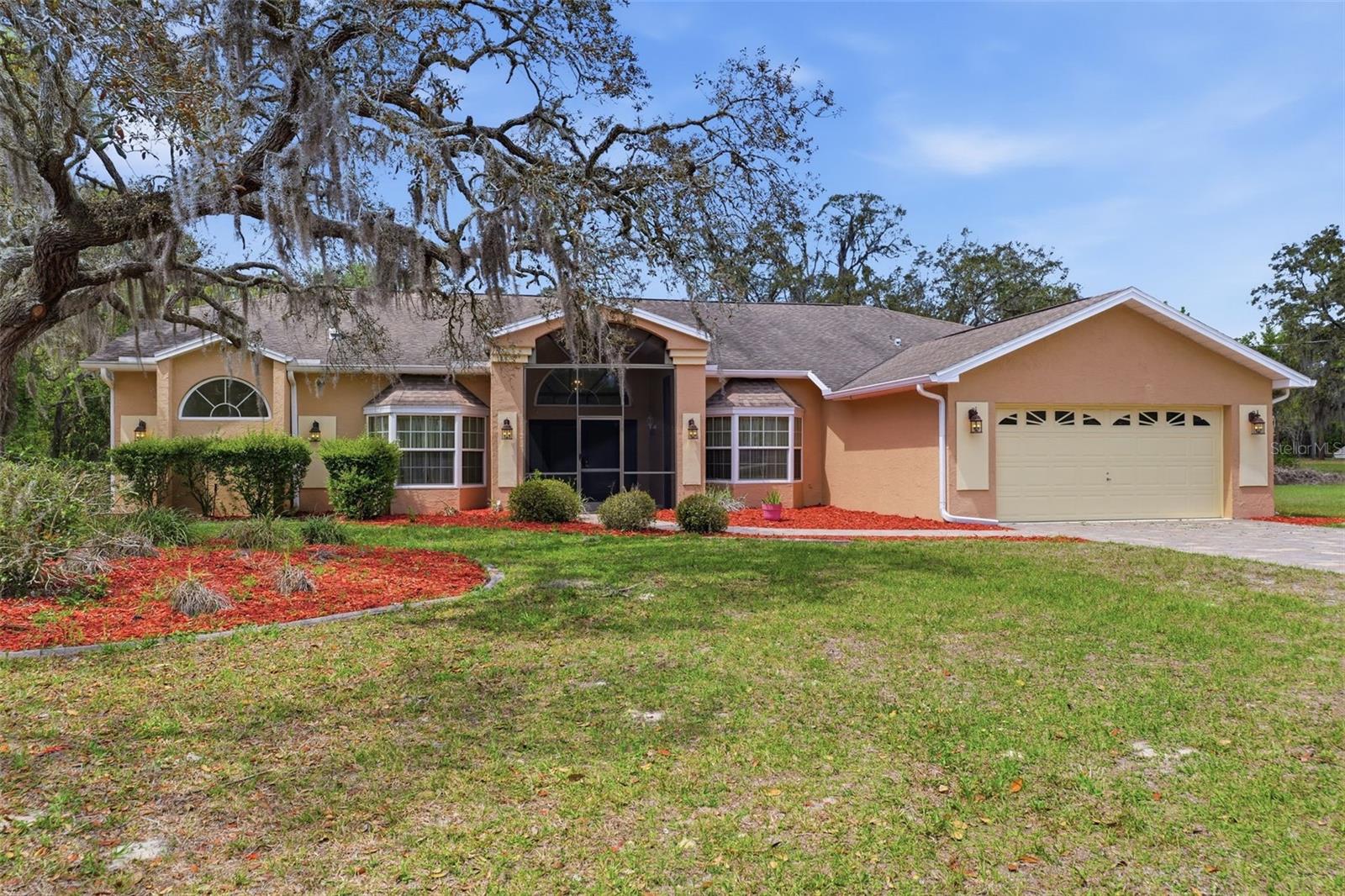 Set on over 3.3 private acres, this expansive estate offers space, functionality, and the kind of indoor-outdoor lifestyle that defines Florida living, complete with 3 bedrooms, 3 bathrooms, a dedicated office/den, 2-car garage, pool, outdoor kitchen, separate outdoor bath, and a massive workshop with electricity. A circular driveway and additional front and rear parking pads provide ample space for vehicles, including room for an RV or camper near the workshop. The home welcomes you with a grand, fully screened and covered front porch with soaring ceilings, leading through double doors into an impressive foyer where the formal dining room sits to the right and wood-look laminate flooring flows through the dining room, living room, and office. Straight ahead, the expansive living room features vaulted ceilings, a wood-burning fireplace with stone accents, and four French doors flanked by windows that flood the space with natural light. The open-concept kitchen is both spacious and functional, offering white tile floors, white cabinetry, a closet pantry, double ovens, a breakfast bar, and a central cooking island, all connected to a bright breakfast nook with a full wall of windows and plantation shutters. The office/den is thoughtfully designed with double French doors and a charming window seat. The primary suite is generously sized and features large windows, a walk-in closet, and a private French door leading directly to the in-ground hot tub area, while the ensuite bath includes white tile, a double vanity, a step-in shower, and a raised soaking tub positioned beneath a window as a focal point. The second bedroom offers two built-in closets and an ensuite bath with a single vanity, window, and step-in shower, with convenient access from the main living area. The third bedroom features sliding glass doors leading directly to the covered porch and pool area. The outdoor living space is truly exceptional, with an expansive pavered lanai that is partially covered and includes a built-in outdoor kitchen with sink and stove, seamlessly connecting to a wooden deck with an in-ground hot tub and a screened pool area, all designed for entertaining and relaxation while overlooking the large backyard and wooded surroundings. A third full bathroom is located in the pool area and includes a tub/shower combo, built-in shelving, and a single vanity. The indoor laundry room offers corridor access between the home and garage and features a utility sink and wall-to-wall cabinetry for storage. At the rear of the property, the oversized metal workshop with electricity provides incredible versatility for hobbies, storage, or additional vehicle space. Located in Spring Hill, this property offers convenient access to the Suncoast Parkway for an easy commute to Tampa, as well as proximity to Weeki Wachee Springs State Park where you can kayak in crystal-clear spring waters, the Withlacoochee State Trail for biking and outdoor recreation, and a short drive to the Gulf Coast for boating, fishing, and waterfront dining, making this a rare opportunity to enjoy privacy, space, and convenience all in one.