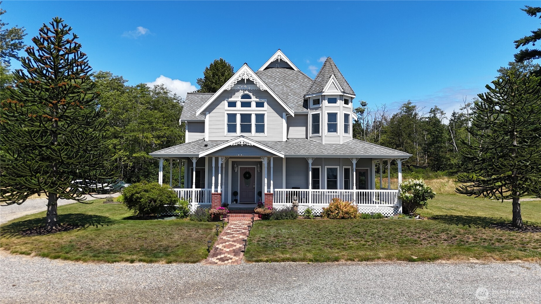 Set on 8 private acres, this custom-built Victorian-style home offers over 3,000 sqft with 3 BD & 3.25 BA. Thoughtful details throughout include a welcoming foyer, winding staircase, crown molding, Anderson windows, chandeliers & built-in surround sound. The main level features a library with custom built-in cabinetry, spacious living room with gas fireplace, formal dining room, kitchen with sitting area & second gas fireplace, and a sunroom with access to the backyard patio. Upstairs, the primary suite includes access to a private balcony also shared with one secondary bedroom. Two additional bedrooms are connected by a Jack-&-Jill bath, and a cedar-lined closet provides additional storage. A separate staircase off the laundry room leads to a large bonus room. The attached 3-car garage includes a built-in workbench & 2 freezers that stay. Outside, enjoy the wraparound covered porch and exposed aggregate patio with sea glass & agates embedded throughout. An arbor leads to a detached art studio with a sink, while a separate garden shop with a roll-up door provides room for a riding mower, tools & equipment. A one-of-a-kind property with the space, character & details of a home designed to be enjoyed for years to come.