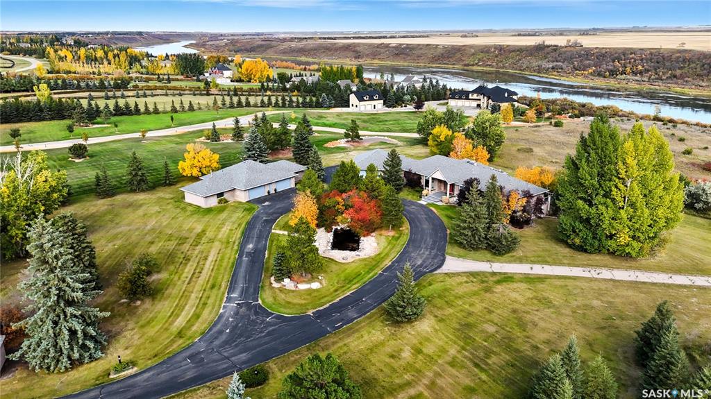 This 3640 sq ft Walkout Bungalow is situated on a 8.8 acre parcel with views of the South Saskatchewan River. With a wonderful location in an active community with rink & play center. Walking into this home, you are welcomed with double-door entry with phantom screens and a spacious foyer leading to an open floor plan with 10 ft ceilings. Great Room features a gas fireplace and custom Redl built-ins, large windows with scenic views. Custom Redl Kitchen is a perfect space with an abundance of cabinets, oversized island with seating, storage, gas cooktop, sink with garburator, granite countertops, baking counter with appliance storage, wall pantry with roll outs, Sub Zero Fridge, built in dishwasher, brand new trash compactor, built-in oven & microwave, coffee bar, dining nook with garden door to composite deck. Formal dining room with a buffet niche. Primary Bedroom is a full retreat with views of the river and access to the deck, gas fireplace with built-ins, dual walk-in closets(1 with stackable washer & dryer), a 4 piece en-suite with in-floor heat, air jet soaker tub, separate shower, dual vanity with granite top & linen closet, sitting area with direct access to basement gym and 3 piece bathroom. Den with a tray ceiling and bayed window.2-piece bathroom with custom stone countertop, laundry room with cabinets, sink, & craft/sewing desk complete the main. Walkout basement features in-floor heat, large family room with 3-way gas fireplace, garden door to covered, partially enclosed patio,games area with wet bar feature seating, fridge,dishwasher & sink. 2 large bedrooms with jack&jill 4- piece bathroom, den/craft room with closet, large mechanical/storage room with wine room. Home is wired for sound system,LED lighting up the driveway, new carpet(2023), new boiler(2023), central vac,4 furnaces & central air, window treatments, & generator for backup power. Attached 8-car heated garage, detached 12-car heated garage/workshop with hoist &cabinets &2-piece bathroom.
