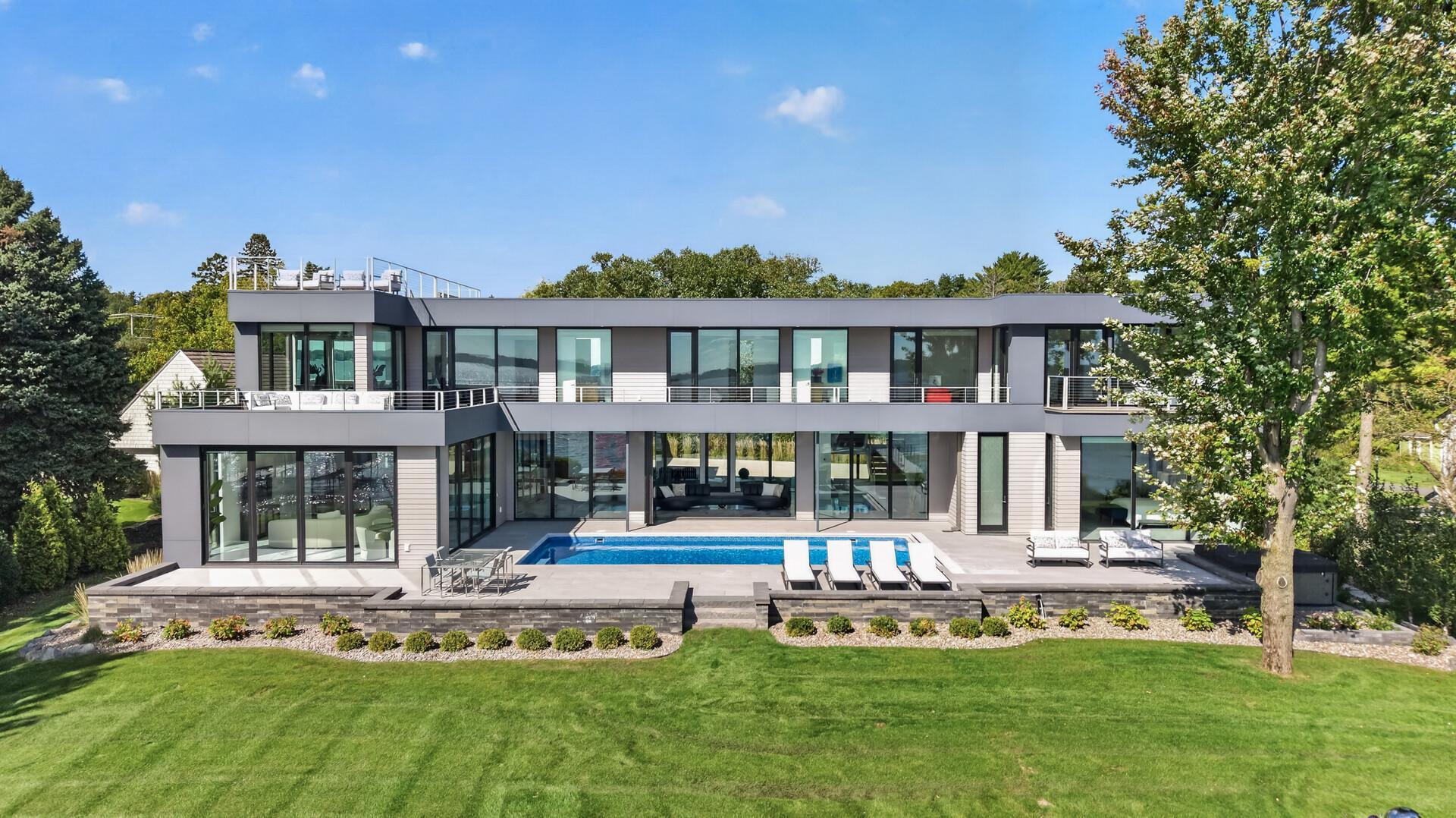 A striking expression of modern lakefront luxury, set along 120 feet of pristine, level shoreline on the coveted shores of Browns Bay. Positioned on iconic Shoreline Drive, this nearly brand-new architectural residence offers over 6,000 sqft of thoughtfully designed living space, where expansive walls of glass frame uninterrupted southern views across Lake Minnetonka and the distinction between indoors and out nearly disappears. A private, resort-like setting just minutes from downtown Wayzata, every element of this home has been intentionally designed to celebrate its extraordinary surroundings. From the moment you enter, the scale, architecture, and quality are unmistakable. Walls of glass and accordion doors bring the lake into the home, while an integrated whole-home Lutron system provides effortless control of lighting and automated window shades, adding another layer of sophistication to the exceptional finishes and craftsmanship throughout. Beautifully landscaped grounds enhance the home’s striking curb appeal and architectural presence from the moment you arrive. The main level is designed for effortless living and entertaining, with expansive gathering spaces, a show stopping kitchen, and seamless indoor-outdoor connection. A spectacular main-level primary suite offers a private escape with a spa-caliber ensuite and custom closet, while the upper level adds an equally beautiful primary suite of its own, along with additional refined living spaces and bedrooms offering flexibility for guests and everyday living. Outside, the architecture takes full advantage of its remarkable setting. An expansive deck spans the entire south side of the home, extending the living space along the water and capturing the home’s sweeping southern exposure. Above, a private rooftop terrace offers another place to take in the setting, whether starting the morning with yoga and coffee or winding down with sunset and panoramic lake views. Walkouts from every bedroom open directly to the outdoors, while the newly redone pool decking surrounds the sparkling pool and overlooks the lake, creating a seamless connection between the home, pool, and shoreline. A statement in modern lakefront living, where exceptional design, extraordinary quality, and an unparalleled setting come together at the highest level.