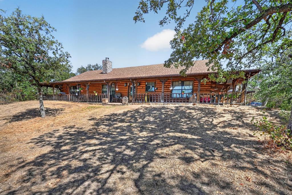 Custom Satterwhite Neches 8in D-log home on 10 acres in Springtown. Built 2003, 2,436 SF, 3BR-2BA, with a full wraparound covered porch and mature oaks. Interior is 90% tongue-and-groove wood with exposed wood beams, alderwood doors, and blue pine and aspen accents in two bedrooms and a bath. Vaulted great room features a Majestic wood-burning fireplace and Velux skylights. Kitchen and primary bath offer custom cabinetry, a reproduction antique-style electric range, and sawn, stained, and sealed concrete floors throughout. Primary suite includes a jetted triangle soaking tub, rain-head and body-jet shower, and dual walk-in closets. 10x24 sunroom addition with a 2-year-old mini-split, two Velux skylights, and tile floor. Wireless home automation and outdoor speakers. New Class 3 CertainTeed roof (May 2026), 3-zone radiant in-floor heat, and a 5-ton heat pump. 25x30 metal garage with two 10x10 roll-up doors, a 4.2kW 48V off-grid solar system (ground-mount sun-seeking and roof-mount panels, 300Ah battery backup), a 220V EV charger, and concrete driveways. Attached 2-car garage plus 2-stall carport, a 12x24 cedar tongue-and-groove workshop with AC and 220V electric, and two 12x12 finished storage rooms. Barn with four finished 10x10 stalls, a 10x10 tack room, water, and 200-amp electric; second drywalled outbuilding with wood floor; a small metal barn and metal shed, both with elec; additional carports throughout the barnyard. Manual backup generator with transfer switch and three separate 200-amp electric services to outbuildings. Private well (~300 ft, Trinity River Basin), aerobic septic with new 2026 controller and aerator, 4-zone WiFi irrigation, 50-gallon Polaris propane water heater, Starlink internet (primary and standby), property-wide security cameras, and gated electric entry. 5 acres cross-fenced with no-climb and 4-board white vinyl fencing plus barnyard pens, suited for horses or livestock. A rare blend of craftsmanship, systems, and acreage.