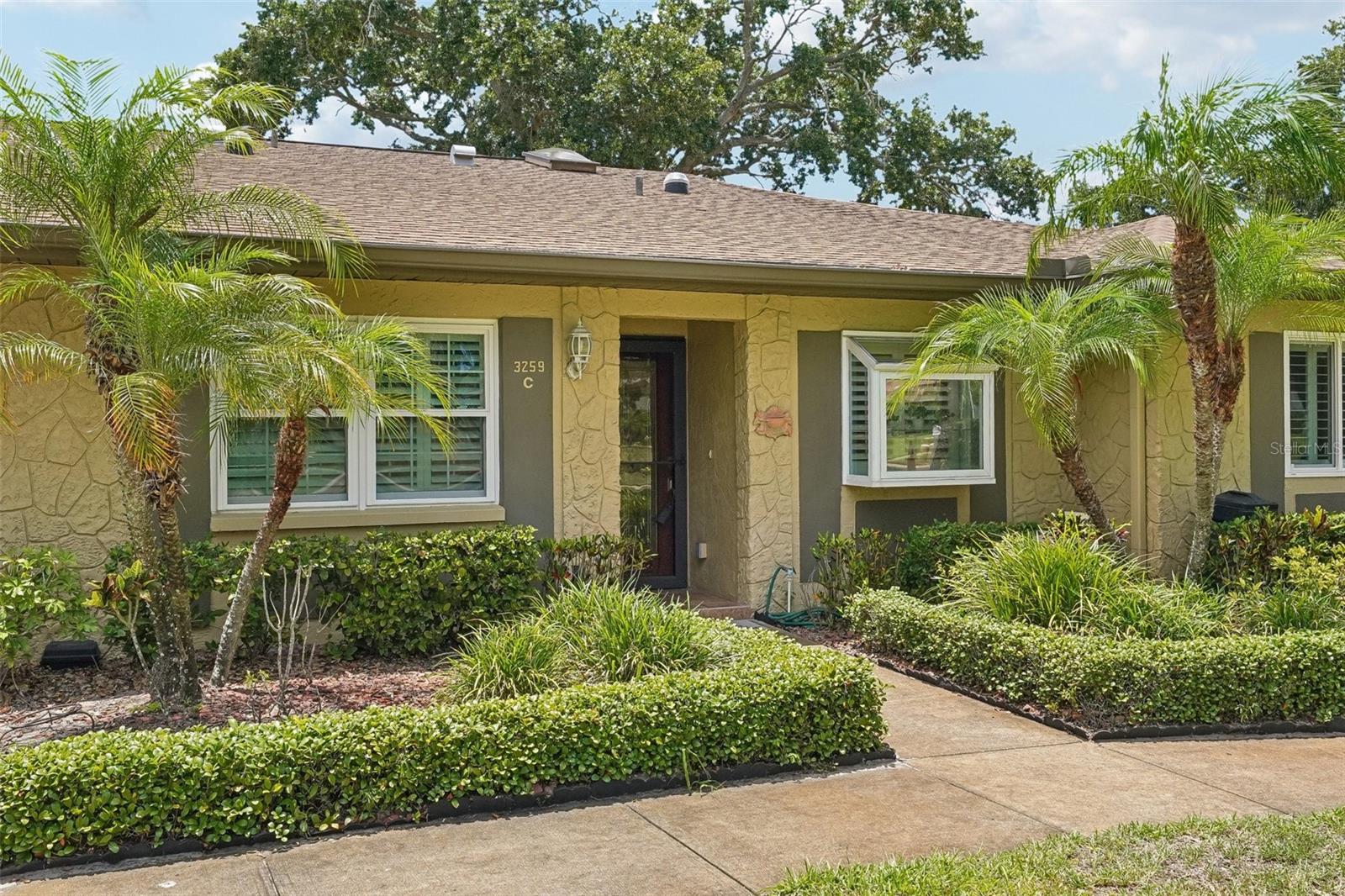 Nestled beneath mature oaks in Highland Lakes, Palm Harbor’s premier 55+ golf course community, this beautifully updated two-bedroom, two-bath villa offers everyday comfort, maintenance-free living, and outstanding resort-style amenities. The home welcomes you in with bright natural light, quality finishes, and thoughtful updates throughout. Hurricane-impact windows add peace of mind, while 3½-inch plantation shutters, large 18-inch tile, engineered hardwood flooring, LumaDome lighting, crown moulding, soft-close cabinetry, and built-in closet systems enhance the home’s style and function. The kitchen makes an immediate impression with high-end custom solid wood cabinetry, soft-close doors and drawers, granite countertops, stainless steel appliances, and a glass cooktop. A breakfast bar with pull-up seating ties into the living and dining areas, creating an easy flow for daily living, casual entertaining, and relaxed gatherings. The primary bedroom offers generous space with two closets, including a walk-in closet, plus an updated ensuite bath with a large double-sink vanity and a beautifully tiled walk-in shower with frameless entry, built-in shelf, and seat. Positioned near the front of the home, the second bedroom adds privacy and sits conveniently beside the guest bath. Both bathrooms are updated with soft-close cabinets and drawers, granite countertops, and Glacier Bay fixtures. Nearby, a dedicated laundry room with storage and utility sink adds everyday convenience. At the back of the home, a sunroom-style flex space features a wall of windows with Key West plantation shutters and a door that opens directly to the paver patio, creating a bright, versatile setting for work-from-home use, morning coffee, reading, or relaxing. The paver patio extends the living space outdoors, shaded by a beautiful oak and surrounded by mature landscaping. With room for seating, dining, grilling, and gathering with friends, it offers a serene setting for enjoying the Florida lifestyle. Highland Lakes is known for its exceptional value and active lifestyle. Low HOA fees include landscaping, building maintenance, trash removal, cable and internet, water and sewer, golf membership with no green fees, and an impressive collection of amenities. Enjoy lighted tennis and pickleball courts, shuffleboard, two pools, including a geothermal Olympic-sized pool, and a clubhouse with a fitness center, billiards room, and auditorium where clubs meet and events are held, all just a short two-minute walk away. Residents also enjoy access to the Lake Tarpon Lodge with a boat ramp, dock, community pontoon boats, secure RV and boat storage, and more. Located in a non-evacuation flood zone and centrally positioned near shopping, dining, medical facilities, and Gulf of Mexico beaches. Don’t miss out on this exceptional home. Schedule your private showing today.