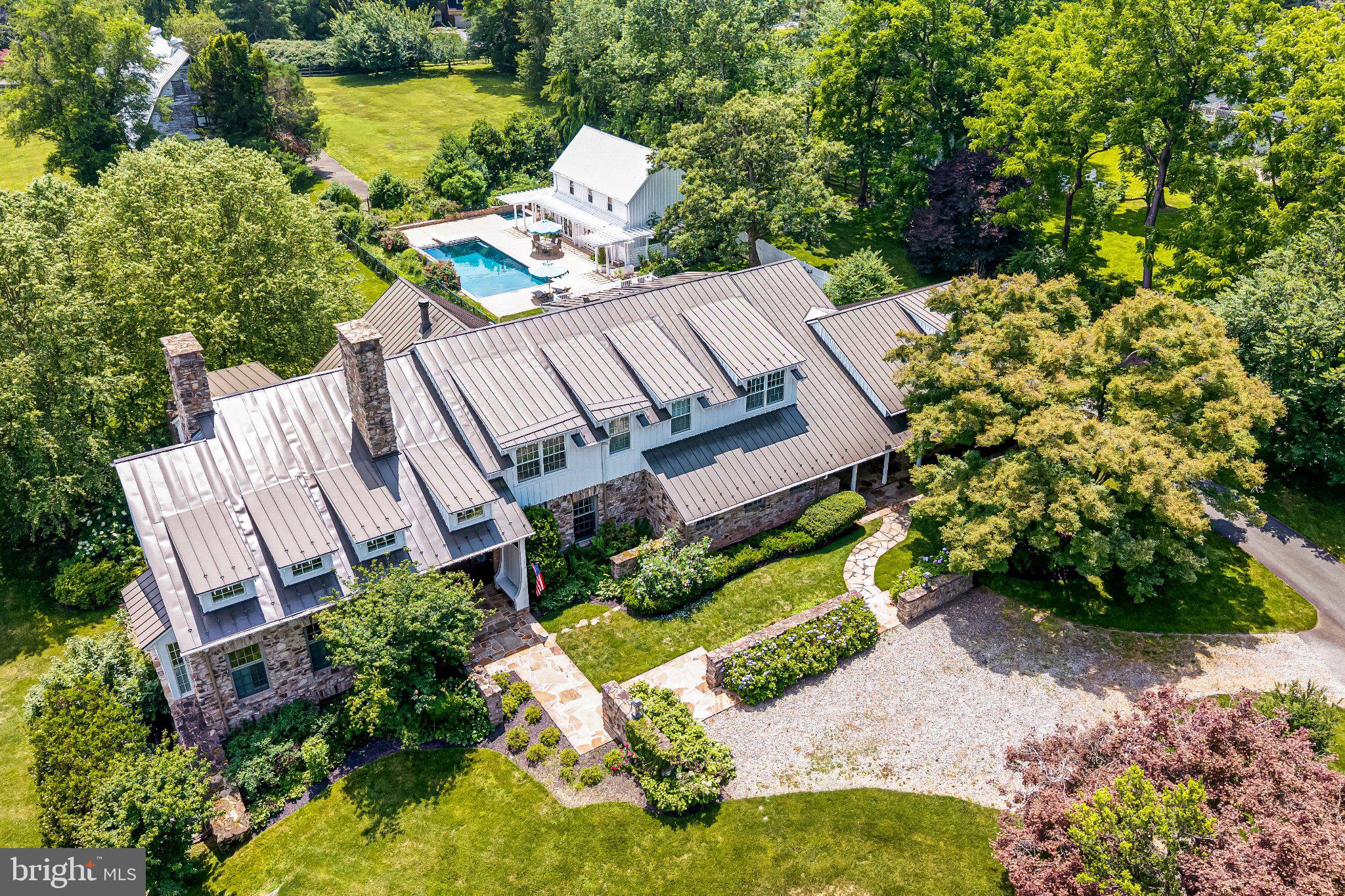 Set on five magnificent acres along one of McLean’s most storied roads, 8133 Georgetown Pike is a modern Virginia farmhouse in the truest sense—crafted for today, rooted in Virginia. Conceived by Lococo Architecture and built by Block Builders Group, the home and its setting are an authentic expression of the Virginia countryside—minutes from everything, yet worlds away from all of it.  Reclaimed oak beams carry the weight of another century. Random-width wood floors, substantial stonework, and custom millwork give the home a sense of permanence. This is a house that could have stood here a century ago—and will belong here for generations to come. The main residence, built in 2013, offers 9,135 sqft, five bedrooms, five full and three half baths, four fireplaces and three garage bays.  The separate three-bedroom, two-bath pool house (first constructed circa 1920) with 1,512 sqft brings the estate to a combined eight bedrooms, seven full baths and three half baths. Inside the main house, heated floors run quietly beneath all three levels, while a double-sided elevator connects them with ease. The main level unfolds the way established homes do - a foyer with presence, a library built for long afternoons, a reading room, formal rooms for occasions and informal ones for Tuesdays, two offices, and a screened porch that bring the outdoors in. Reclaimed beams, stone, handcrafted millwork and built-ins appear throughout, creating rooms that feel elegant and comfortable. The kitchen is where the house begins and ends each day. Honed White Fantasy granite, rustic reclaimed oak over beam, soft green inset cabinetry, a farmhouse sink, and slate floors set the tone, while Viking, Miele and Sub-Zero appliances stand ready. A proper butler’s pantry and oversized food pantry keep the work of entertaining backstage. The mudroom has built-in storage; the laundry room is generous and practical; and a dedicated potting room—with an antique carpenter’s bench, porcelain drainboard sink, reclaimed oak shelving and French doors to the patio—feels like a remnant of an earlier Virginia estate. Upstairs, the primary suite reads like its own address. A sitting area with built-ins gives way to a private screened porch and separate balcony overlooking the grounds. The marble bath offers dual vanities, a soaking tub, a floor-to-ceiling marble shower, heated towel rack, and two private water closets. Generous dressing and closet spaces provide room to settle in. The remaining bedrooms are finished with the same care—walk-in closets, built-ins and en suite baths that make every room feel intentional. Downstairs offers a different perspective with a recreation room anchored by a fireplace with soapstone surround and reclaimed oak mantel, opening directly to the lower stone terrace. A billiard room, an exercise and dance studio, and a full bar designed for real entertaining complete the lower level. Five acres give the property a sense of separation and privacy that is increasingly rare in McLean. Flagstone terraces move naturally into lawn and gardens, while a pergola and wood-burning stone fireplace create an outdoor room of their own. A flagstone path leads to the pool where waterfalls and a hot tub transform the grounds into a private resort. Offering genuine independence for guests or extended family, the pool house features a living area, full kitchen and bath on the main level and three bedrooms with an additional full bath upstairs. A separate rear driveway provides access to adjacent Greenway Heights.Meander further through the gardens and terraces, and the property reveals a former dairy barn which gives the estate something no new construction can replicate—a tangible connection to the Virginia countryside beneath it. Tysons is 3.1 miles away, downtown McLean 3.8 miles, Chain Bridge 6.6 miles and Dulles International Airport 13 miles—placing Washington, Tysons and the wider region comfortably within reach.
