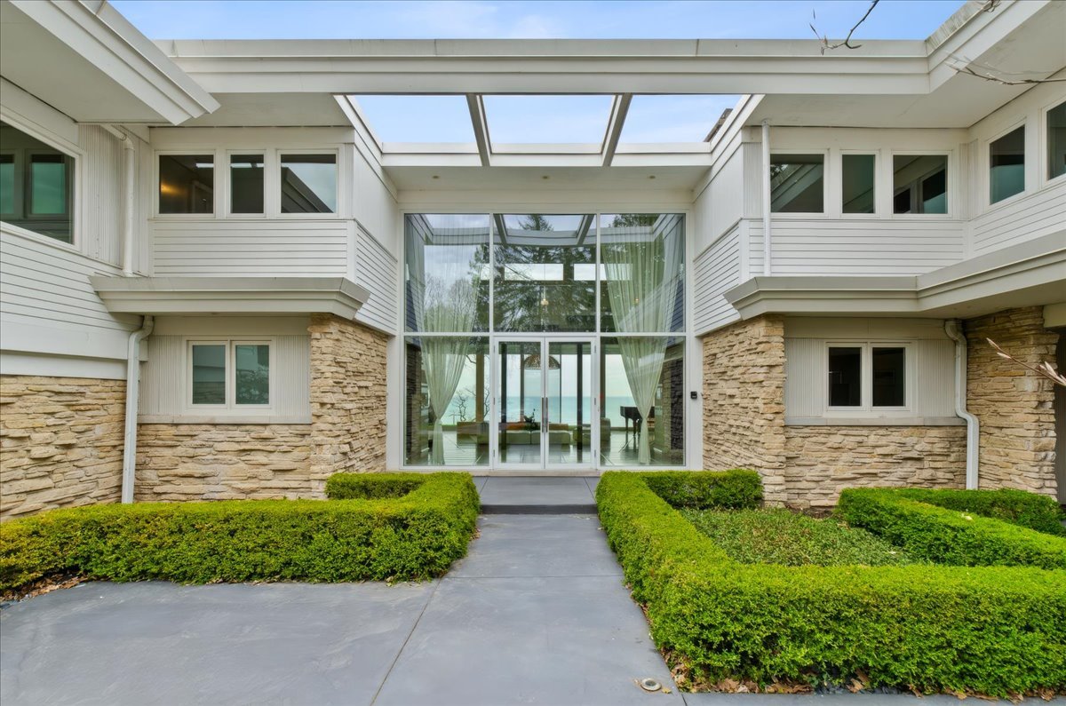 Situated on a prestigious private lane in East Highland Park, this rare lakefront offering is a Mid-Century Modern masterpiece. Designed in 1957 by renowned architect Henry L. Newhouse II for Irving B. Harris, Chicago Philanthropist, this 10,000-square-foot contemporary residence sits on nearly two acres of lush grounds with magnificent, unobstructed views of Lake Michigan. Experience the ultimate wow factor as you enter the dramatic foyer and take in the breathtaking vista. The interior features large expanses of glass and natural light, offering a flexible floor plan that flows effortlessly for entertaining and everyday living. An exquisite foyer leads to custom beveled, imported French Limestone floors and dramatic floor-to-ceiling windows that frame the water. With minimalistic aesthetic, the Chef's Eat-In Kitchen is finished with custom black walnut cabinetry, a wall of granite, gourmet appliances, and a sleek gas fireplace. The home's expansive footprint includes a main floor Primary Bedroom Suite with a secondary Primary Suite on the 2nd level and seven additional Ensuite Bedrooms, providing unparalleled space and privacy. Despite significant renovation since construction, the home still retains the core architectural integrity and mid century character established by Newhouse. For wellness and recreation, an Indoor Pool Pavilion features a Dectron temperature-controlled system, a retractable clerestory roof, a steam room, and a dedicated second kitchen equipped with Viking appliances. Outside, the tranquility of the lakefront setting takes center stage. A sparkling Outdoor Pool overlooks the water, while a private tram and stairs lead down to 150 feet of secluded beach. This is a unique opportunity to own a significant piece of architectural history with unlimited potential on the shores of Lake Michigan!