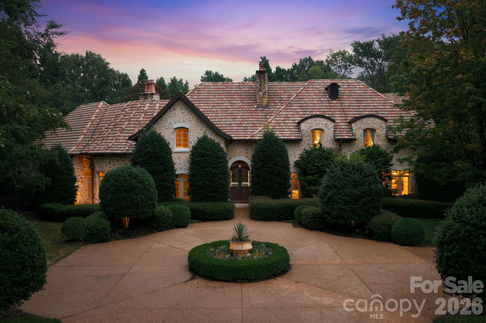 A timeless expression of European architecture, this exceptional Morrocroft estate is privately positioned behind the gates of one of Charlotte’s most coveted communities. Set on 1.18 acres of meticulously landscaped grounds, the residence blends enduring craftsmanship with refined contemporary updates, creating a home that is both grand in scale and remarkably inviting. A stately stone façade and classic terracotta roof introduce interiors where heated natural stone floors, custom millwork, soaring ceilings, and abundant natural light define every space. Thoughtfully designed for effortless entertaining and comfortable everyday living, the main level features an elegant primary suite, beautifully proportioned gathering spaces, and a chef’s kitchen complete with premium appliances, an oversized island, prep kitchen, and adjoining wine cellar. Walls of glass open to a private outdoor retreat where a resort-style pool and spa, expansive covered terraces, and lush mature landscaping create an atmosphere of complete serenity. Wellness and recreation are equally prioritized with a dedicated fitness studio, sauna, and flexible garage space designed to accommodate vehicle lifts for the automotive enthusiast. Perfectly balancing timeless architecture with modern functionality, this one-of-a-kind residence offers exceptional privacy, distinguished design, and an unmatched lifestyle just moments from Charlotte’s premier shopping, dining, and business districts.