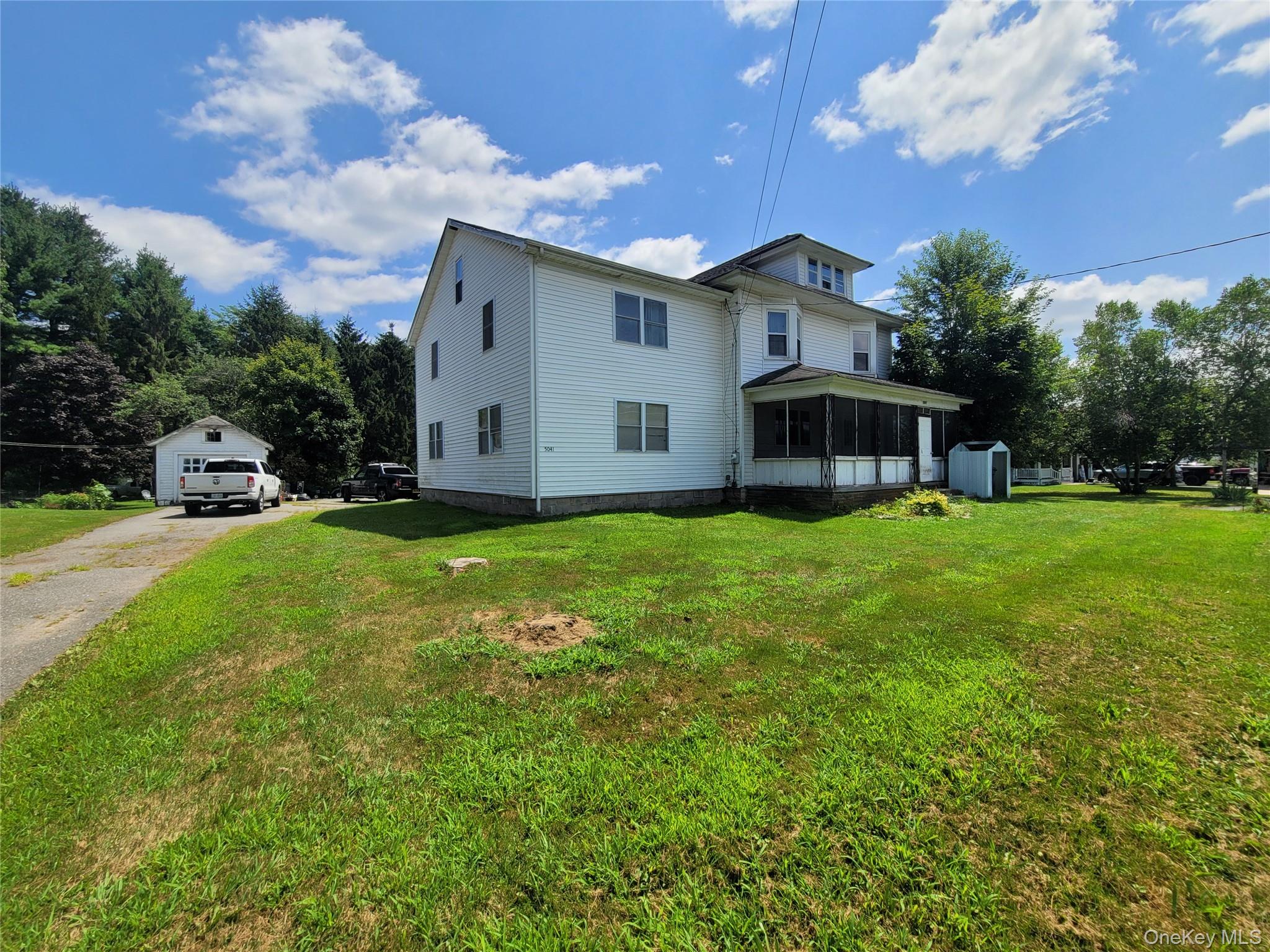 Rear view of house featuring a sunroom, an outdoor structure, a lawn, and driveway