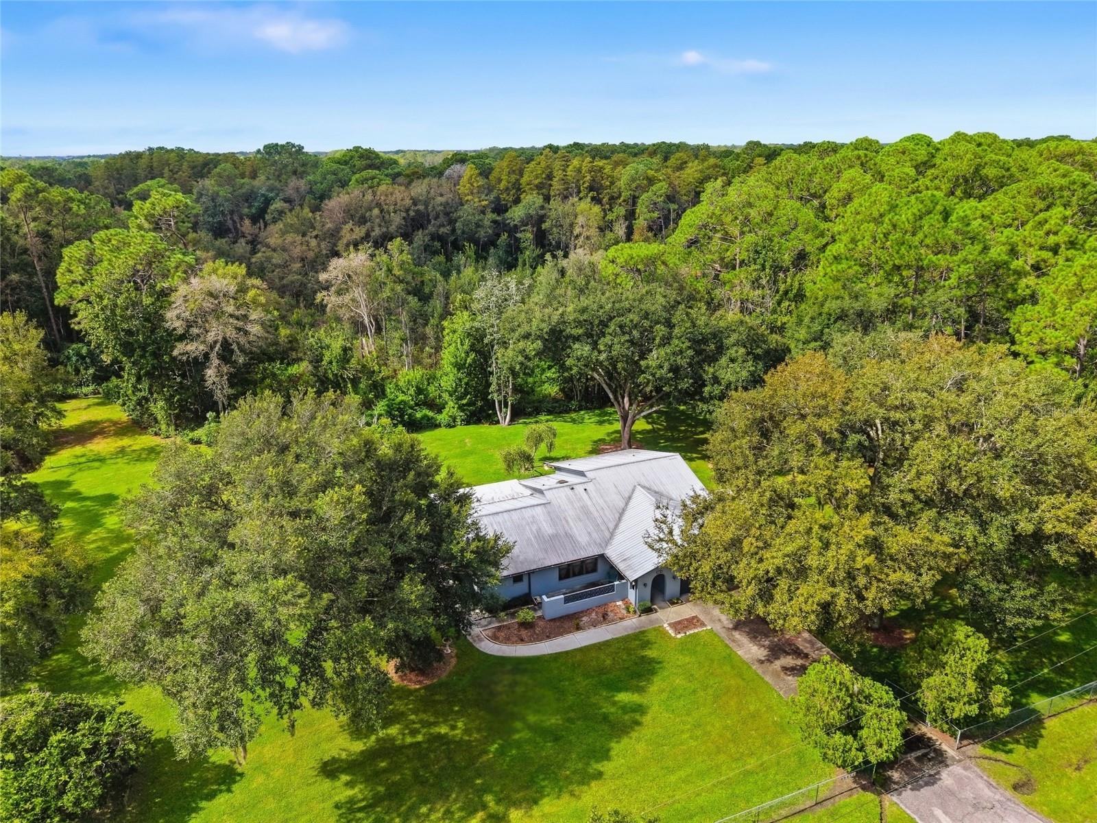 Looking for a rare chance to own acreage with conservation, privacy, wildlife at your doorstep, and room to spread out? Look no further! This beautifully maintained ranch-style home sits on 5.52 acres of Florida serenity, backing to protected conservation land. From the moment you arrive, the mature oak canopy and lush, park-like grounds set the tone for peaceful country living just minutes from everyday conveniences. Step through the front door and you're greeted by a coat closet and access to the two-car garage. To the left is a formal living room, versatile enough to serve as an office, with the dining room just beyond. The kitchen and breakfast nook connect to the family room. A wet bar area in the family room adds a wonderful touch for hosting family and friends. This split-bedroom floor plan offers privacy. The generously sized primary suite features two closets, a walk-in shower, and sliders that open directly to the screened back porch. On the opposite side of the home, two additional bedrooms share a spacious bathroom with a tub, and the back bedroom overlooks the preservefor its own peaceful view. With a dedicated laundry room with a sink and several linen closets, there’s no shortage of storage throughout. Outside is where this property truly shines. The sliding doors at the back of the home lead you out to the screened back porch overlooking the most breathtaking backyard view with a sprawling, private lawn giving way to natural conservation with a small pond. There's plenty of room here for animals to roam, and the wildlife is simply unmatched: deer, sandhill cranes, hawks and songbirds, turtles, rabbits, and even the occasional fox make regular appearances. Grab your morning coffee or evening glass of wine and listen to the birds while soaking in one of the most peaceful views around. Peace of mind comes standard here, with major updates already taken care of: well has been replaced, metal roof (December 2007), HVAC (May 2021), Rheem water heater (May 2021), dishwasher (June 2021), refrigerator (2021), garbage disposal (November 2023), plus newer sinks and a newer guest bathroom toilet with bidet. Call today for your private showing.