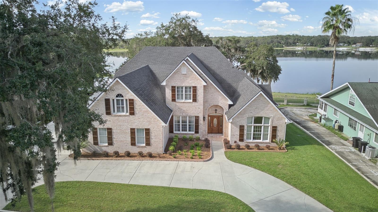 Tucked behind the gates of an intimate three-home lakefront enclave, this extraordinary custom-built estate on Cowpen Lake is the kind of property where generations can gather, traditions can begin and weekends have a way of turning into weeks. Whether envisioned as a full-time multigenerational home or a treasured family vacation retreat, this one-of-a-kind property offers remarkable space, privacy and versatility across two parcels totaling approximately 1.11 acres with 125 feet of lake frontage. At its heart is an impressive 4,759-square-foot custom brick residence with 6 bedrooms and 5.5 baths, thoughtfully designed for entertaining while remaining warm and inviting for everyday life. High ceilings, graceful architectural arches, plantation shutters, expansive gathering spaces, a gas fireplace and walls of windows create a light-filled interior that draws your attention toward the lake. The kitchen is truly the heart of the home, with rich wood cabinetry, granite counters, abundant prep and storage space, a large center island with seating, stainless steel appliances and an impressive Viking professional-style gas range and hood, ready for everything from holiday dinners with the entire family to pancakes before a day on the water. The kitchen flows into generous dining and living areas so the cook never has to miss the conversation. The spacious main-floor primary suite is its own private retreat, with room for a sitting area, beautiful lake views, an oversized walk-in closet and a substantial bath featuring dual vanities and an impressive walk-in shower. Additional bedrooms (two en suites) give family and guests room to spread out, while the oversized upstairs bonus/game/billiard room is ready for movie nights, game days and a little friendly competition. Main home also has a 27 KW generator for added comfort. Outside is where the Florida lake lifestyle truly comes alive. Relax on the covered lakefront porch beneath its beautiful wood-clad barrel-vaulted ceiling, surrounded by mature trees and wide-open water views, and imagine morning coffee as the lake wakes up, long family dinners outdoors and cocktails at sunset. Cowpen Lake is a multipurpose recreational lake ideal for boating, fishing and water skiing, and your private boat ramp means the next adventure can begin right from home. Car collectors, boating enthusiasts and hobbyists will appreciate an attached three-car garage plus an extraordinary detached six-car garage/workshop with a full bath, offering exceptional room for vehicles, boats, equipment, toys and projects. A separate 1BR/1BA, 676-square-foot guest residence with its own kitchen, bath, laundry and private entrance makes this property especially well-suited for multigenerational living, extended family and visiting friends, allowing everyone to enjoy their own space while still being together. With two wells, two septic systems, no association fees and a wonderfully private lakefront setting, this is more than a home. It is a place for family and friends to gather around the kitchen island, spend afternoons on the water and end the day together on the porch. Some furnishings may also be negotiated, creating the opportunity for a truly move-in-ready experience, whether you plan to make Cowpen Lake home year-round or simply arrive with your bags packed for weekends, holidays and summers at the lake. Some properties are simply places to live. This one feels like a place your family could return to for generations.
