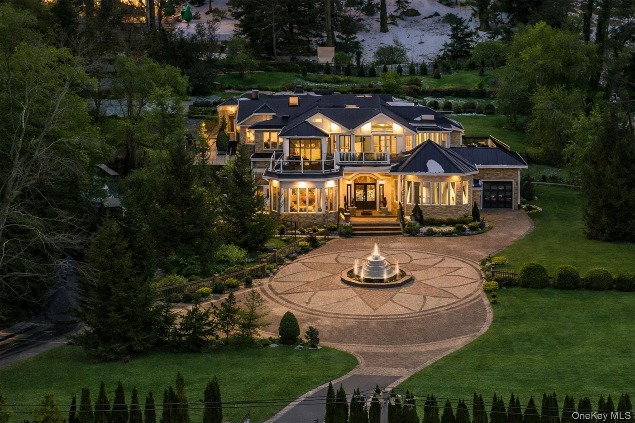 Perched on a sprawling acre in the prestigious Village of Kings Point within the award-winning Great Neck School District, this extraordinary waterfront estate offers breathtaking panoramic views of Manhasset Bay and a lifestyle reserved for the most discerning buyer. Behind electric security gates, a grand circular driveway with fountain accommodates over a dozen vehicles, setting the tone for the elegance that awaits. Private beach access, in-ground pool, hot tub, luxurious outdoor lighting, expansive decks and patios create a true resort-style retreat designed for unforgettable entertaining. Enter through oversized double doors into soaring 12-foot ceilings, exquisite custom millwork, and a stunning foyer with circular staircase. The main level features a dramatic formal dining room, separate living room with fireplace, and a spectacular chef’s kitchen with double granite islands, butler’s pantry, top-of-the-line appliances, and captivating water views from nearly every angle. A first-floor bedroom with full bath offers ideal guest or extended living accommodations. Elevator access services all floors, including the expansive upper level highlighted by oversized entertaining spaces, a theater room with wet bar, private office, and a magnificent primary suite reminiscent of a Four Seasons retreat with spa-inspired bath, soaking tub, and grand stone shower. Complete with whole-house entertainment system, recessed speakers, EV charging station, and refined modern upgrades throughout, this timeless Kings Point waterfront masterpiece delivers unmatched privacy, prestige, and panoramic beauty — a rare opportunity to own one of the North Shore’s most impressive addresses.