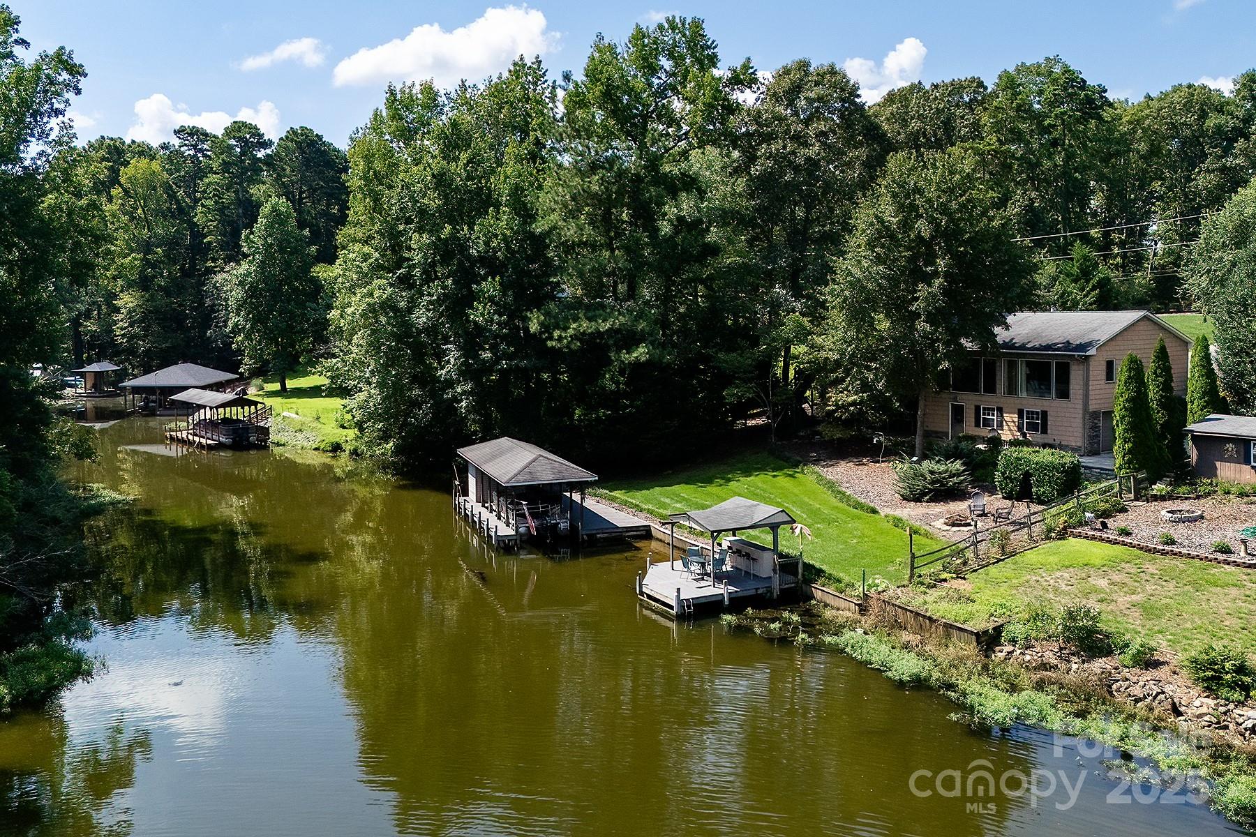 Experience the perfect blend of elegance and relaxation in this secluded Lake Tillery getaway that comes mostly furnished. Nestled in a private setting with gorgeous landscaping, this home offers serene water views and outdoor spaces designed for relaxation, including a 1-slip boathouse, gazebo, and two large screened porches overlooking the lake. The main-level great room boasts large windows framing the view, while the primary suite features tall wood ceilings, generous closets, and a spa-like bath with dual-head walk-in shower, jetted tub, double sinks, and granite counters. The spacious kitchen shines with Brazilian granite countertops and amazing layout! The basement is perfect for entertaining with a dry bar, mini fridge, and microwave, plus a large workshop and extra garage workspace. Cozy yet airy, this home blends comfort and elegance, creating the ultimate lakefront retreat.