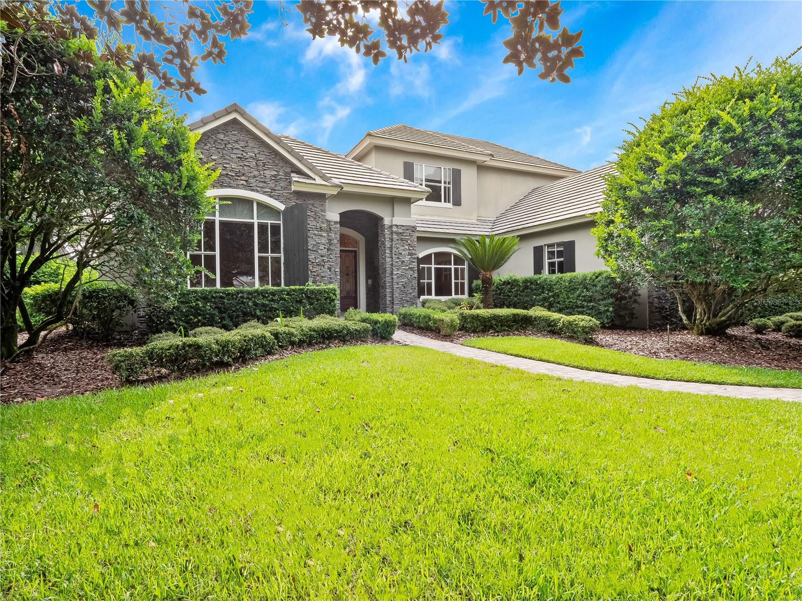 One or more photo(s) has been virtually staged. Welcome to this beautiful residence in the highly sought-after Alaqua Lakes community where thoughtful design and timeless elegance meet everyday comfort. Nestled on a private ½-acre lot with a spacious backyard, this home offers exceptional curb appeal with its inviting exterior elevation and striking stone accents. Inside, you’ll find soaring ceilings, quality finishes and generous living spaces that blend sophistication with warmth and character.

At the heart of the home lies the gourmet kitchen designed to inspire both everyday living and elevated entertaining. Overlooking the family room and the bright and airy sunroom, the kitchen is a true gathering space filled with natural light and seamless functionality. Just steps away are the formal and casual dining areas, a 1,200-bottle climate-controlled wine room and a butler’s pantry making hosting effortless and stylish.

A dedicated office with custom built-ins and a cozy fireplace offers the ideal setting for remote work or a quiet study. The grand primary suite, located on the first floor, serves as a private retreat with a spa-like en suite bath featuring split vanities, granite countertops, dual sinks, a whirlpool soaking tub, and two spacious walk-in closets. Upstairs there are three generously sized bedrooms and two full bathrooms that provide comfortable accommodations for family or guests along with plentiful storage throughout.

Set within a premier golf course community, residents enjoy world-class amenities including clay tennis courts, a resort-style pool, a 24-hour guard-gated entrance and enhanced community security. Ideally located near Central Florida’s best attractions, upscale shopping and dining, major highways, and international airports, this exceptional home delivers a rare combination of luxury, privacy, and lifestyle.
