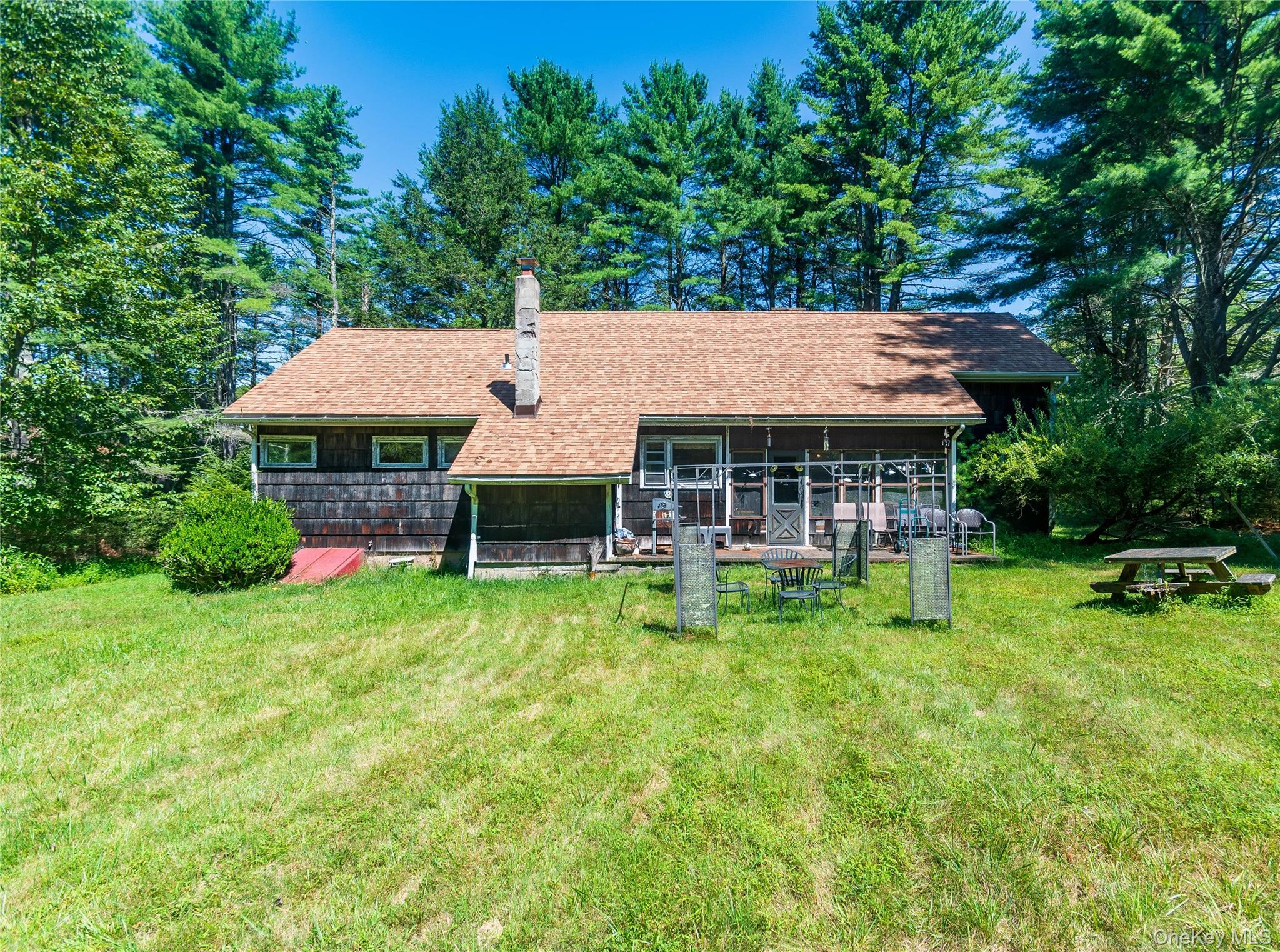 Rear view of property with a chimney, a lawn, a shingled roof, and view of scattered trees