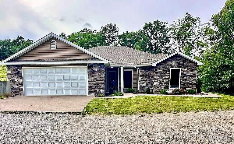 Single story home with stone siding, driveway, an attached garage, and a front lawn