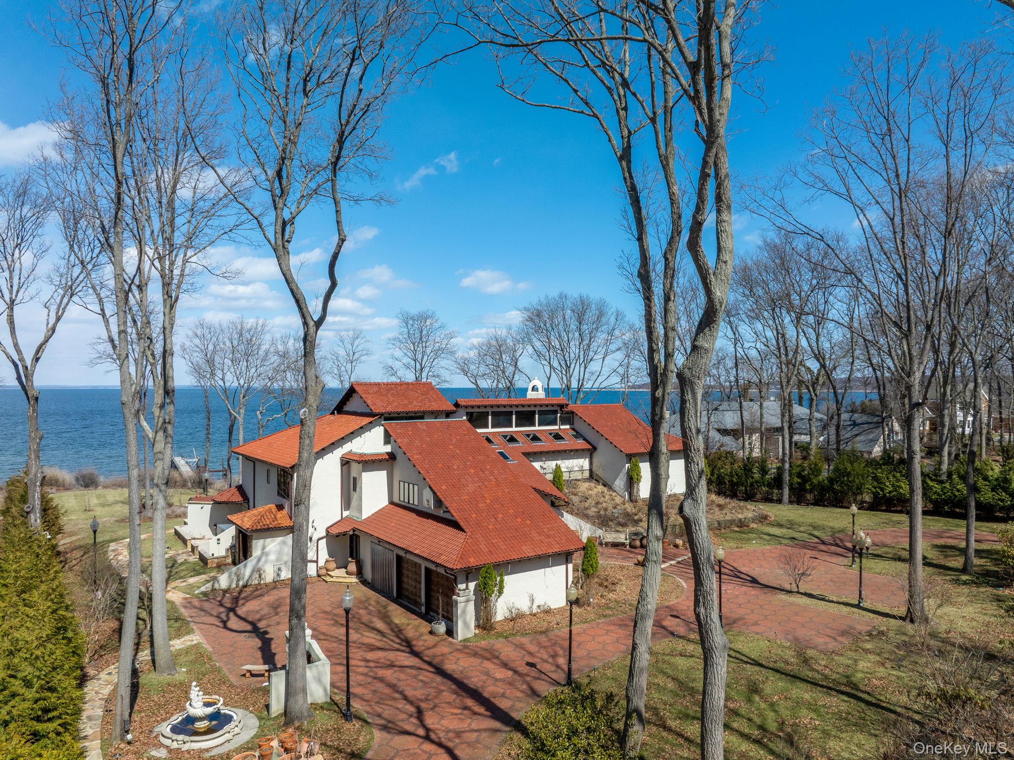 Perched along the shores of the Long Island Sound, 1 Sea Crest Drive is a spectacular Mediterranean-style waterfront estate offering breathtaking views, refined craftsmanship, and exceptional amenities designed for luxurious coastal living. Grand double wood doors open to a dramatic foyer where floor-to-ceiling windows frame sweeping water views and the private, deep-water dock beyond. The light-filled entry sets an elegant tone with a gracious staircase leading to the second-floor catwalk, which separates the private primary wing from the home’s four additional bedroom suites. An elevator and powder room are conveniently located just off the foyer. Designed for both everyday living and elegant entertaining, the main level features a chef’s eat-in kitchen with Wolf appliances, double ovens, a True refrigerator, dual sinks, and quartz countertops. Just off the kitchen, the laundry room is thoughtfully designed with a Shaws farm sink and brass fixtures. The water view dining room, highlighted by marble floors and French doors, captures stunning views and opens seamlessly to the outdoor setting. The impressive great room showcases soaring floor-to-ceiling windows, parquet wood floors, and a striking fireplace, creating a warm yet dramatic gathering space. A separate bar room with its own fireplace offers an inviting setting for entertaining, while the indoor pool overlooking the Sound brings resort-style living indoors year-round. Additional first-floor features include a private office and a spiral staircase leading to the spa-inspired primary bath, complete with sauna and jacuzzi tub. The primary suite itself is a serene retreat, featuring a fireplace, marble flooring, and French doors opening to a waterside deck. Cedar closets add another thoughtful luxury. Across the elegant catwalk, four additional en-suite bedrooms provide comfort and privacy, including two with spectacular water views. A rear staircase leads to the three-car garage, with direct access back into the kitchen and laundry area.Set on a prized waterfront parcel in Lloyd Harbor, the property’s deep-water dock and panoramic Sound views create an extraordinary setting for boating, entertaining, and enjoying the very best of waterfront living. Deep-water dock. Endless views. A truly exceptional Lloyd Harbor offering.