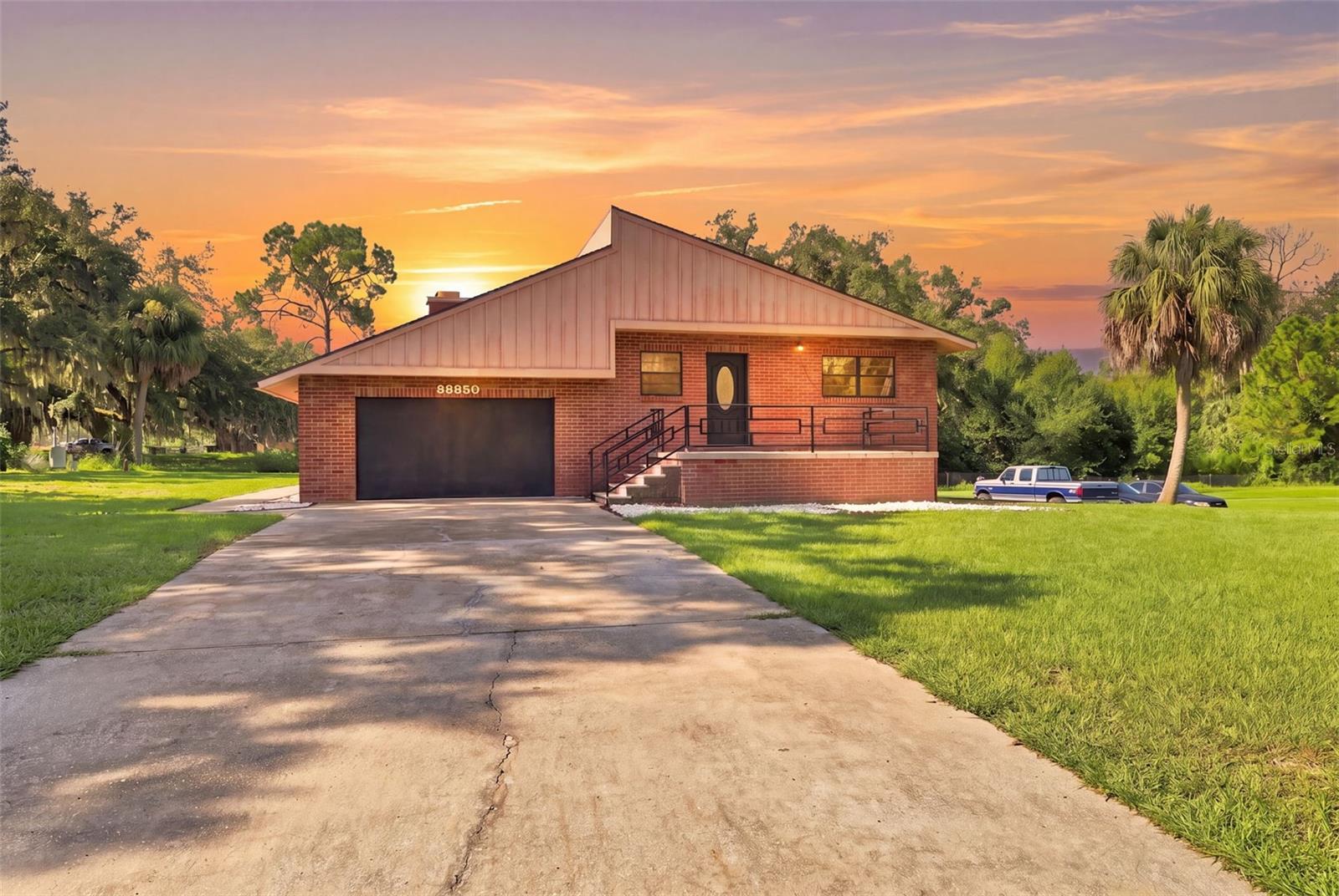 Spread across 1.44 acres with expansive lawn space and mature trees, this distinctive 4-bedroom, 4-bath home offers an additional 1,804 sq. ft. of finished basement space, providing an impressive amount of room for living, entertaining, and everyday versatility. A 2021 roof and 2022 water heater add to the home's appeal, while the brick exterior and elevated covered entry create a welcoming first impression. Inside, the kitchen offers tile flooring, white cabinetry, granite countertops, stainless steel appliances, a dual-basin sink beneath a window, and a wide breakfast bar connecting easily to the dining area. Nearby, the spacious dining room provides room for gatherings and French doors leading toward the screened patio. Step down into the impressive lower-level family room, where tile flooring, a dramatic vaulted ceiling with exposed wood beams, and a striking floor-to-ceiling dark stone wood-burning fireplace create one of the home's most memorable gathering spaces. Bedrooms 2 and 3 offer comfortable accommodations with natural light and built-in closets, while the exceptionally spacious primary suite features tile flooring, contrasting accents, ceiling beams, a large closet, and plenty of room for a sitting area. Its private bathroom includes black cabinetry, a dual-sink countertop, two mirrors, a walk in shower, frosted window and more. Bedroom 4 also offers tile flooring, a large closet with distinctive red louvered doors, and direct access to an adjoining bathroom with a red vanity, granite countertop, and tub/shower combination. A spacious laundry and utility room adds everyday functionality with extensive built-in cabinetry, open shelving, washer and dryer connections, and water treatment equipment. Step outside to the large covered and fully screened patio, offering generous space for outdoor dining, entertaining, or relaxing while overlooking the surrounding greenery. Sliding glass doors and French-style doors connect this inviting area to the interior, while steps lead to the expansive backyard. A detached enclosed gazebo provides another place to unwind and enjoy views across the property, while the long concrete driveway, mature oaks, palms, and broad lawn areas provide plenty of outdoor space for recreation or gardening. Conveniently located near shopping, dining, parks, recreation, and everyday amenities, this property combines space, character, and versatility in a peaceful setting.