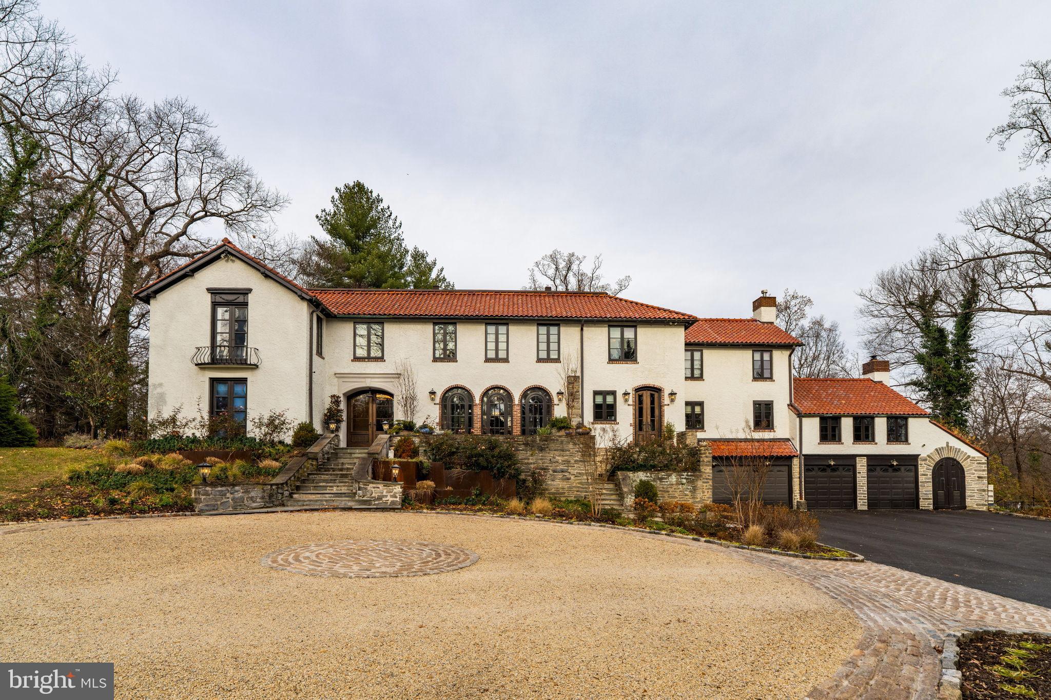 Privately set along a quiet lane in Northside Haverford, just moments from the historic Merion Cricket Club, this exceptional residence has been fully renovated with an unwavering focus on craftsmanship, materials, and architectural detail. The result is a home that honors its European-inspired heritage while seamlessly delivering refined modern luxury and everyday functionality.A circular drive and stone approach lead to the striking stucco façade, clay tile roof, arched openings, and iron detailing. Inside, a dramatic, wide foyer with custom tile flooring and a grand double staircase creates an immediate architectural statement, offering both scale and symmetry rarely found.The first floor unfolds into a series of beautifully defined and generously proportioned spaces. The formal living room features a fireplace and custom built-ins, while a sunlit first-floor office just beyond offers abundant natural light and exceptional functionality. The well-sized dining room, complete with a working fireplace, flows effortlessly into a front sunroom with a bar and direct porch access—ideal for entertaining or relaxed daily living.At the heart of the home, the kitchen is both striking and highly functional. Stunning marble countertops, custom cabinetry, a statement Lacanche range, and a Sub-Zero refrigerator anchor the space. Large glass doors open directly to the rear patio and pool, creating seamless indoor-outdoor flow. A beautifully designed butler’s pantry provides exceptional storage, prep space, and support for entertaining.Adjacent to the kitchen, the great room impresses with vaulted ceilings, exposed wood beams, a fireplace, and a nearby full bath, offering flexible use as a living space, guest area, or potential first-floor suite. Toward the rear, a true showstopper awaits—an extraordinary media and entertaining room with wood-beamed ceilings and a projector-screen television, perfectly designed for movie nights, game days, or large gatherings while opening to the terraces beyond.Upstairs, the primary suite is privately situated and thoughtfully designed as a peaceful retreat. The bedroom features beautiful wood ceiling detailing, while the spa-inspired bath includes a freestanding soaking tub, oversized glass-enclosed shower, patterned tile floors, and custom vanities. A boutique-style dressing room with extensive custom cabinetry, integrated lighting, seating, and a stone-topped center island completes the suite.Secondary bedrooms are spacious and well-appointed, complemented by a conveniently located second-floor laundry room and a dedicated workout or wellness space.The finished lower level continues the home’s thoughtful design with a recreation area, custom mudroom, and a full bath featuring a second laundry and a shower ideal for a dog wash.Outdoors, the property transforms into a private, resort-style retreat. Expansive stone terraces overlook a custom pool with raised spa, outdoor kitchen, and multiple seating and dining areas. Café lighting, terraced gardens, walking paths, and a tucked-away fire pit lounge create a serene, estate-like setting, while a gated entrance, fully fenced yard, mature landscaping, new irrigation system and wooded surroundings provide exceptional privacy.A rare Northside Haverford offering defined by architectural integrity, extensive renovation, and exceptional indoor-outdoor living.