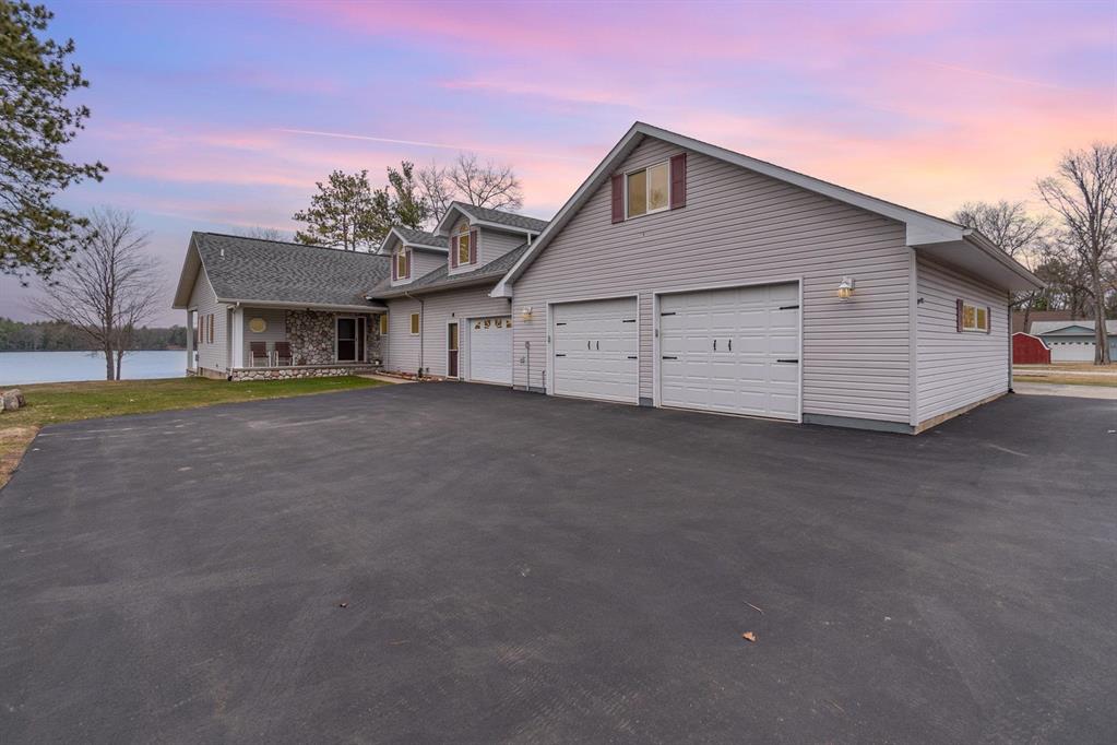 Stunning Lakefront Custom Home with Sunset Views on Round Lake! Welcome to this beautifully maintained and thoughtfully designed custom-built home, nestled on 80 feet of prime frontage on Round Lake, which connects to Indian Lake-offering over 300 acres of spring-fed, sandy-bottom waters perfect for boating, swimming, and world-class fishing. Built in 2002 and packed with upgrades, this west-facing home captures breathtaking sunset views from nearly every room. A two-level deck spans the entire waterfront side of the property, with an additional level above a spacious cinder block storage building-ideal for storing all your water toys. The lakeside covered patio features overhead lighting and ample electric outlets, perfect for entertaining or installing a future hot tub. Step inside and be greeted by a warm knotty pine cathedral ceiling, a gas fireplace, and open-concept living, kitchen, and dining areas with panoramic lake views. The kitchen boasts custom cabinetry, and brand-new carpet (2024) enhances the living room, hallway, and primary bedroom. The main floor offers two bathrooms, each with large walk-in showers with built-in seating. The spacious primary suite includes a walk-in closet and private access to the patio. A second bedroom features matching custom cabinetry, while the large laundry room offers even more storage, a counter for folding, and deep sink. What was once a single-car garage has been converted into a unique multipurpose room, equipped with a second kitchen-perfect for canning, hobbies, or entertaining. This space connects to the attached two-car garage, outfitted with commercial-grade pallet racking for ultimate storage. Upstairs, two staircases (one from the garage, one inside the home) lead to an open loft currently used as a third bedroom and office area. Beyond the loft, discover a fourth bedroom with full bath, and a fifth bedroom ideal for guest quarters, complete with a sitting area. Don't let this one get away.