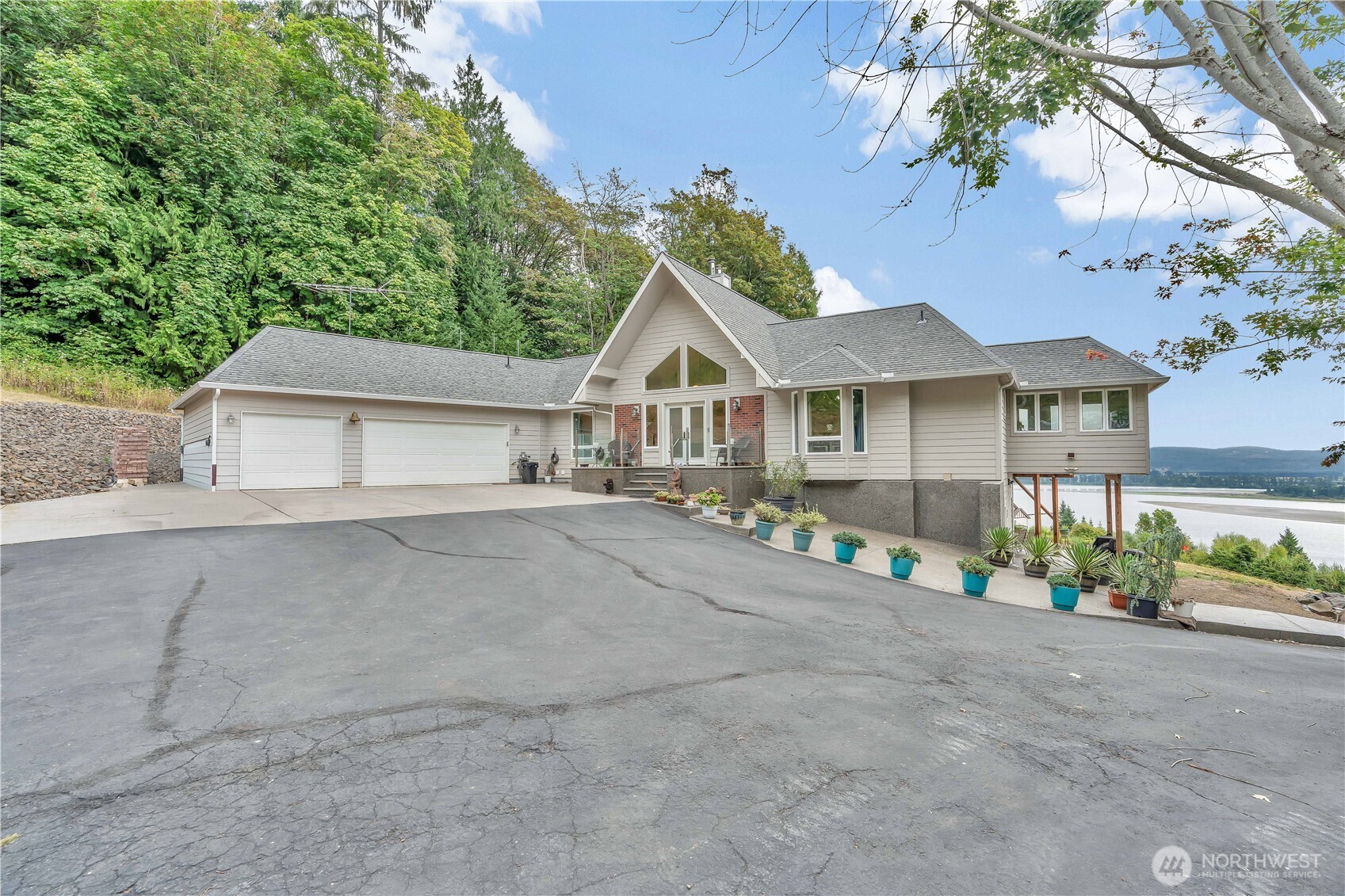 Gorgeous two-level home showcasing breathtaking views of the Columbia river and surrounding woods, with abundance of natural light and beautiful view from nearly every room. A welcoming French-door entry opens to the main level, hardwood floors, soaring vaulted ceilings, and dramatic floor-to-ceiling windows create an impressive yet comfortable living environment. The expansive deck and patio provide exceptional spaces to take in the scenery, entertain, or simply relax. The oversized kitchen offers abundant workspace, a large island, dedicated eating area, and sliding doors that open directly to the deck. A spacious laundry room and ceiling fans throughout much of the home add everyday convenience. The primary suite features a luxurious ensuite bath with double sinks, walk-in shower, and soaking tub positioned beside a window overlooking the stunning view—an ideal place to unwind.The lower level offers a generous family room plus three additional bedrooms, each featuring wall-to-wall carpet and ceiling fans. A second kitchen with industrial-grade appliances adds incredible versatility, ideal for extended living, entertaining, hobbies, or other lifestyle needs. Significant upgrades include a new shop/workshop and advanced heating systems.Outside, enjoy an oversized garage, RV parking, expansive workshop, huge deck, and spacious patio. Surrounded by mature woods and incredible lake views, this unique property offers space, flexibility, and an exceptional setting.