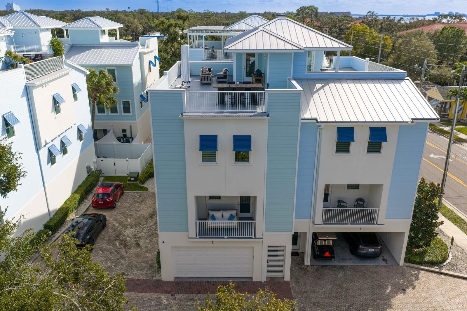 Exquisite Coastal Townhome with Rooftop Terrace and Gulf Views in Dunedin!  Discover refined coastal living in this architecturally stunning four-story townhome, boasting 3 bedrooms + office, 2.5 bathrooms and a Private 4-stop Elevator, perfectly positioned across from the Gulf in coveted Dunedin. Constructed with Insulated Concrete Forms (ICF) for superior strength, energy efficiency, and soundproofing, as well as Miami Dade Impact windows and doors, this residence blends modern craftsmanship and security with timeless elegance. The exterior showcases Hardy siding to ensure lasting beauty and durability as well as 2 balconies (front and back) – 1 featuring a wood-paneled ceiling and a charming porch swing that conveys with the home. 4-car garage with pebble epoxy floor has two separate bays with dual garage doors — the rear section thoughtfully outfitted as a home gym. Behind the private gated entry with rich wood ceiling, the interior features 10-foot ceilings, 8-foot solid-core interior doors, and designer finishes creating an ambiance of upscale sophistication throughout the home. The second floor reveals a bright and expansive great room ideal for entertaining, with defined living and dining spaces that flow seamlessly to the gourmet kitchen. This chef’s space features premium shaker-style cabinetry with crown molding, granite countertops, stainless steel appliances (including a 5-burner gas range), spacious pantry, and a generous center island with seating. Wide-plank engineered wood flooring and ample natural light throughout, enhance the home’s modern coastal style. Dedicated home office provides a quiet and functional space ideal for remote work or creative pursuits. Upstairs, the huge primary suite offers a serene retreat complete with sitting area, spacious walk-in closet and spa-inspired en suite bath boasting dual vanities, tile floor, large soaking tub, and a separate shower. Two additional bedrooms (1 featuring a Murphy bed and built-in desk), a well-appointed full bath with tub/shower combo and a convenient laundry closet, complete this level.  The fenced backyard offers a private outdoor retreat with a paver patio, low-maintenance turf lawn, and beautifully designed landscaping that enhances both style and relaxation. The crown jewel of this exceptional home is the fourth-level Rooftop Terrace — an entertainer’s dream showcasing panoramic 360-degree views of the Gulf, Caladesi Island and Dunedin. Enjoy unparalleled sunsets and gentle sea breezes from your substantial rooftop sanctuary, easily accessible via private elevator and stairs.  Located just steps from the scenic Pinellas Trail and moments from Downtown Dunedin’s acclaimed restaurants, boutiques, and waterfront attractions, this home delivers the perfect fusion of luxury, location, and lifestyle.