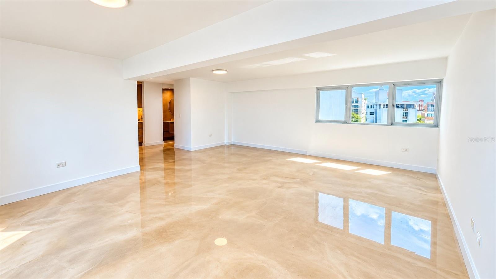 At 1360 Ashford Avenue in Condado, Residence 903 offers approximately 1,140 square feet with two bedrooms, two full bathrooms, and one covered, assigned parking space.Broad windows bring natural light into the living and dining areas, framing views across the neighborhood with glimpses of the Atlantic. Polished floors, warm wood-toned cabinetry, and a neutral palette establish a cohesive interior. The kitchen features streamlined cabinetry, veined countertops, and under-cabinet lighting. The bathrooms continue the material palette with floating vanities, warm-toned tile, and contemporary fixtures.An Ashford Avenue address places the residence within Condado’s established urban coastal setting.