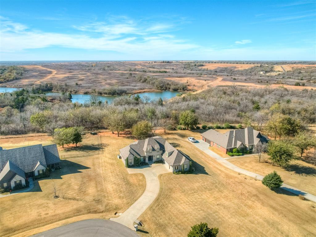 New in Norman. Nestled on a 1.2 acre lot in the prestigious gated community of Manor Lake Hills you'll find this gorgeous 4 bedroom, 3.1 bathroom, 3-car garage home is the perfect blend of comfort and sophisticated elegance. Through the front door you are welcomed with an open concept main living area featuring soaring ceilings, an abundance of natural light and wood flooring. The appointed study sits to the left of the front entry, elegant formal dining room to the right and is open to the main living area boasting cathedral ceiling with wood beams,  a stone fireplace harnessed by custom shelving and built-ins. The kitchen is a chef's dream with butcher block island for additional seating, granite countertops, ample cabinet storage, gas range, 2 ovens, refrigerator and dining space. The secluded primary retreat is spacious with beamed tray ceiling and spa like bathroom offers separate vanities, walk-in shower and soaking tub. The expansive primary closet has numerous hanging rods, shelving, built-in cabinets, drawers, full length mirror and flows into the laundry room with utility sink and storage. Thoughtfully located opposite of the Primary suite are the secondary bedrooms and shared bathroom with tub/shower combo bolstered by separate vanity spaces. Upstairs you will find a wet bar with sink and microwave, secondary bedroom, bathroom, and bonus or game room. Safe room is located in downstairs secondary bedroom. The oversized 3-car garage has clearance to accommodate larger vehicles. The large back patio with fireplace is the perfect space for entertaining or relaxing in the evening. With serene views of the pond, proximate to the neighborhood pool and clubhouse, this beautiful home offers all the convenience of modern living and a peaceful retreat from city life.