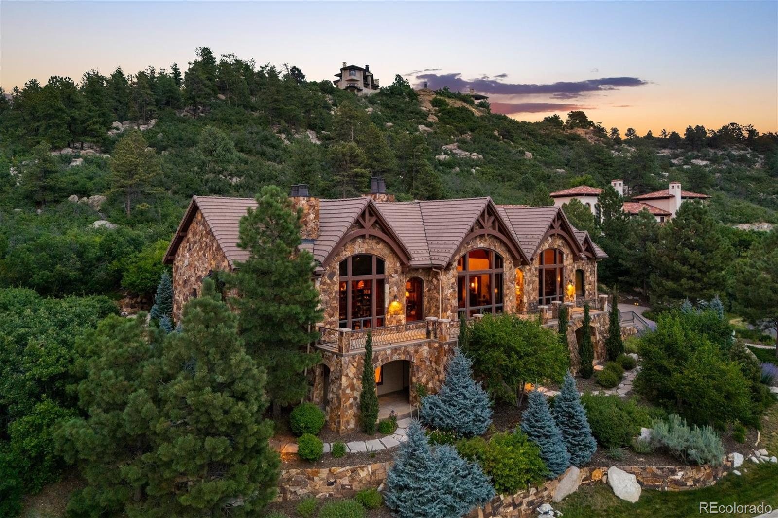 Commanding rare, sweeping views from the Sangre de Cristo Range to Mt. Evans, this 5 bedroom | 9 bathroom estate, regally perched above the gated Village at Castle Pines community, is magnificent in both scale and design. Unfolding around a breathtaking 2-story great room, vaulted ceilings, hand-hewn wood beams, and natural Colorado stone set a tone of grandeur for this impressive home. Designed to entertain, the comfortable family room, with access to the amply sized back patio and yard, offers a seamless transition into the kitchen which is anchored by an oversized island, Sub-Zero refrigerator, Wolf double ovens, and range. Gatherings are further enhanced by a wet bar, formal dining room, and butler’s pantry with dedicated appliances. The fully wood-paneled executive office is fit for a CEO, and the main level is completed by a spacious primary bedroom and spa-like bathroom, ideally located guest suite, second office, two powder rooms, laundry room, and 4-car garage. A destination of its own, the walkout lower level includes a recreation room and bar, soundproof theater, and an extraordinary, climate-controlled wine cellar paired with an adjoining tasting room, both crafted for collectors. An en suite bedroom, workout room with sauna and shower, bonus room, powder room, and abundant storage complete this level. The upstairs is its own retreat with a loft and two additional bedrooms complimented by en suite baths, each with heated floors. The thoughtfully engineered 6-inch steel-reinforced concrete driveway with snowmelt system on the downhill approach and front steps is a plus. Outside, incredible living spaces abound whether you're stargazing by the fire pit on the back patio, playing in the yard, winding through the flagstone paths, dining on the lower level porch, or taking in the spectacular mountain views from the front terrace. Simply put, this exceptional estate is a residence like no other and offers a phenomenal setting for year-round Colorado enjoyment.