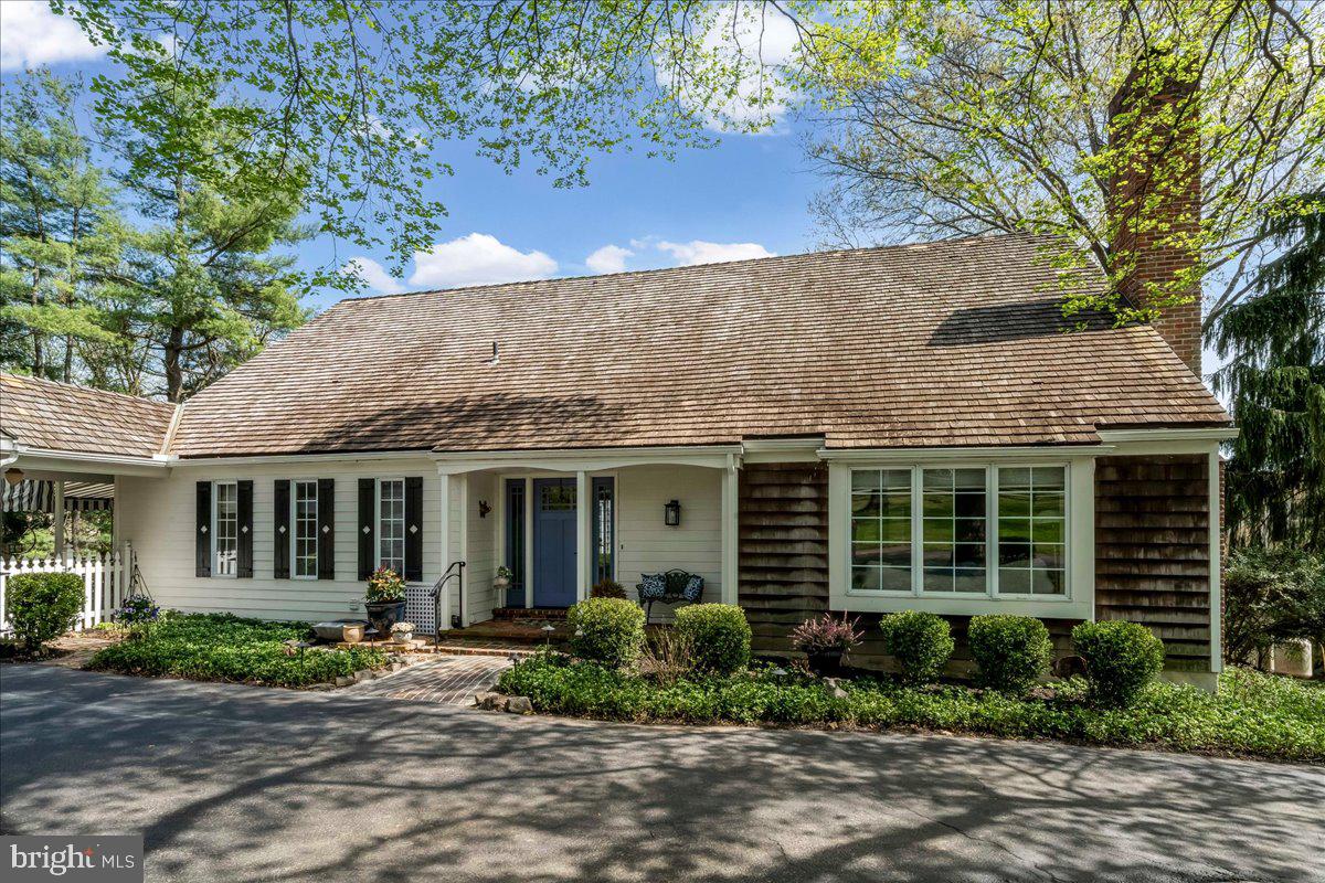 Enjoy the ease of first-floor living in a truly special setting. Custom designed by Ann Capron and built by Bentley, this distinctive cedar shake home blends timeless elegance with effortless comfort. Enter into a charming Philadelphia brick foyer, leading into a spacious, sun-filled living room. The dining room features a wall of windows and French doors to a secluded deck with beautiful views—perfect for entertaining. A cozy den, with vaulted ceiling and wood-burning brick fireplace adjoins the rare first-floor primary suite, which features a row of windows, gorgeous bath, and generous closets. The primary suite shares the dining room deck for a peaceful retreat.  The spacious gourmet kitchen is designed for casual living, featuring an eat-in breakfast or intimate sitting area.  Step outside to an awning-covered patio and large open deck that create your own private oasis. A coat closet, powder room and laundry/mudroom round out the first floor. On the second floor, an airy loft—ideal for a home office—overlooks the den, and two additional bedrooms flank a full bath. Surrounded by mature trees and lush, thoughtfully designed plantings, the property offers exceptional privacy. A circular driveway and two-car garage complete this exceptional home. Ideally located just minutes from the Devon Horse Show, shopping, transportation, and top-rated schools, this home offers the perfect balance of privacy and convenience.