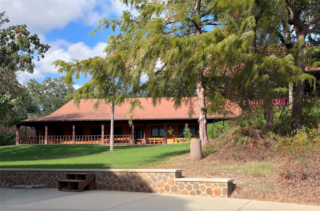 Custom Satterwhite Neches 8in D-log home on 10 acres in Springtown. Built 2003, 2,436 SF, 3BR-2BA, with a full wraparound covered porch and mature oaks. Interior is 90% tongue-and-groove wood with exposed wood beams, alderwood doors, and blue pine and aspen accents in two bedrooms and a bath. Vaulted great room features a Majestic wood-burning fireplace and Velux skylights. Kitchen and primary bath offer custom cabinetry, a reproduction antique-style electric range, and sawn, stained, and sealed concrete floors throughout. Primary suite includes a jetted triangle soaking tub, rain-head and body-jet shower, and dual walk-in closets. 10x24 sunroom addition with a 2-year-old mini-split, two Velux skylights, and tile floor. Wireless home automation and outdoor speakers. New Class 3 CertainTeed roof (May 2026), 3-zone radiant in-floor heat, and a 5-ton heat pump. 25x30 metal garage with two 10x10 roll-up doors, a 4.2kW 48V off-grid solar system (ground-mount sun-seeking and roof-mount panels, 300Ah battery backup), a 220V EV charger, and concrete driveways. Attached 2-car garage plus 2-stall carport, a 12x24 cedar tongue-and-groove workshop with AC and 220V electric, and two 12x12 finished storage rooms. Barn with four finished 10x10 stalls, a 10x10 tack room, water, and 200-amp electric; second drywalled outbuilding with wood floor; a small metal barn and metal shed, both with elec; additional carports throughout the barnyard. Manual backup generator with transfer switch and three separate 200-amp electric services to outbuildings. Private well (~300 ft, Trinity River Basin), aerobic septic with new 2026 controller and aerator, 4-zone WiFi irrigation, 50-gallon Polaris propane water heater, Starlink internet (primary and standby), property-wide security cameras, and gated electric entry. 5 acres cross-fenced with no-climb and 4-board white vinyl fencing plus barnyard pens, suited for horses or livestock. A rare blend of craftsmanship, systems, and acreage.