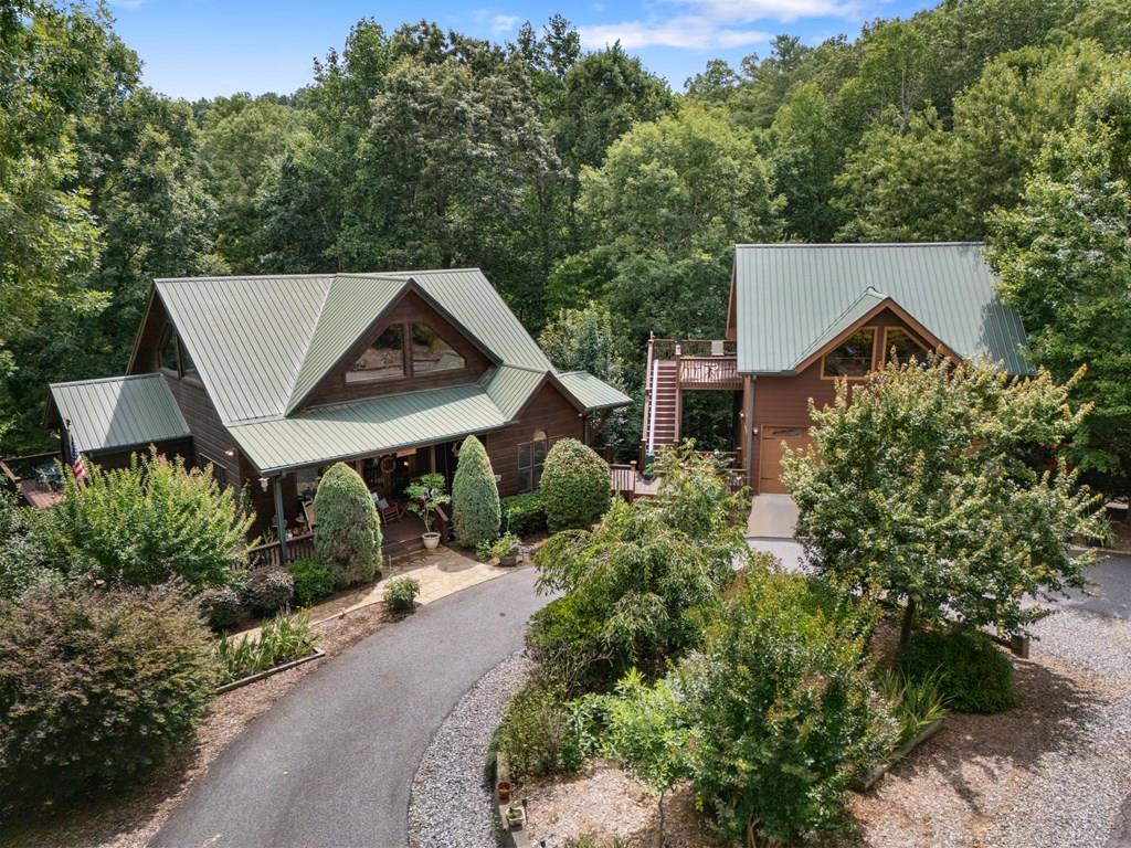 Stunning Spacious North GA Mountain Retreat with Unique Architecture & Modern Amenities! Nestled in a serene setting, this expansive approx. 3,684 sq ft home offers a perfect blend of luxury, comfort & unique design. Arrive via a circular driveway to a spacious covered deck that sets the tone for this remarkable property. Main Level: Step inside to soaring 2 story ceilings, exposed beams & distinctive architecture that define the open-concept living space. The great room, complete w/ a cozy fireplace, flows seamlessly into the dining room & modern kitchen, creating an inviting atmosphere for entertaining or relaxation. The master suite on this level features a generous walk-in closet & a luxurious en-suite bathroom w/ a jacuzzi tub & shower. Step outside to an elevated covered deck, connected to a large, open entertainment side deck, offering breathtaking views of vibrant seasonal plantings & trees. Loft Level : Ascend to the loft level, where a spacious bedroom w/ a walk-in closet & private bathroom awaits. The open sitting area overlooks the great room below, creating a cozy yet airy retreat. Lower Level: The lower level is designed for versatility & comfort, featuring a bedroom w/ a walk-in closet, a full bathroom, a den, & a spacious recreation area w/ a convenient wet bar. This level opens to a lower patio, complete w/ a hot tub & firepit, overlooking a beautifully terraced backyard w/ seasonal views. Three-Story Garage & Additional Living Space: Connected to the main house by decks and walkways, the 3 story garage is a standout feature. The main level offers a 2 car garage w/ ample storage. Above, a stunning 548 sq ft open room w/ cathedral ceilings, hardwood floors, a bathroom & a large closet serves as an ideal guest suite or studio. The lower level offers an additional car bay & a workshop w/ built-in cabinets & stained pine tongue-and-groove walls. Adjacent to the garage, a concrete basketball half-court adds a fun, active touch & abundant parking.
