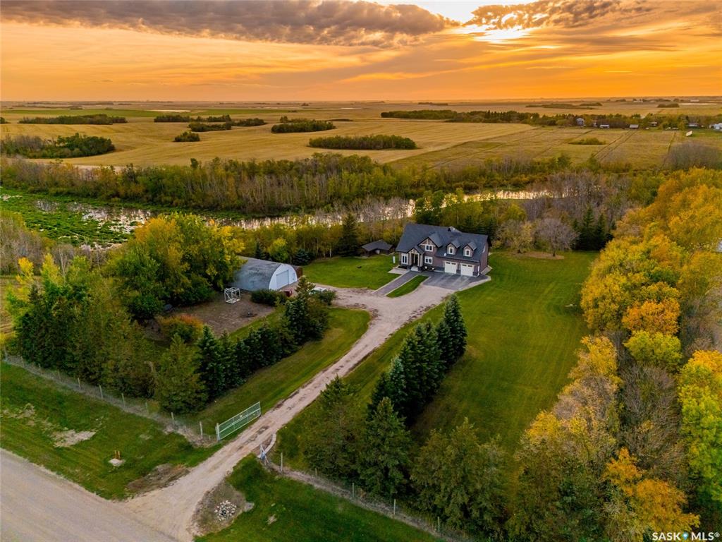 Hidden among mature trees just minutes north of Osler, this custom-built Pawluk Homes property feels more like a private country estate than a typical acreage. Groomed trails wind through the property, fruit trees are scattered throughout, page-wire fencing surrounds the grounds, and a natural coulee along the back creates a landscape that feels established, secluded and completely removed from subdivision living. The home itself was built on a grand scale, but with a floor plan that is anything but ordinary. The main level is open, warm and architectural, with hardwood and tile flooring, a gas fireplace and open railing that connects the spaces without losing definition. Then there’s the primary suite — unusually and thoughtfully located on the main floor. It features a substantial walk-in closet and five-piece ensuite with dual sinks, corner jetted tub and tiled shower. Upstairs is where this home really breaks away from the expected. Two bedrooms and a four-piece bath are joined by an incredible bonus room measuring over 600 sq. ft. — a space large enough to completely reinvent depending on how you live. The walkout basement adds even more potential, with nine-foot ceilings, in-floor heat, two bedrooms already framed and a bathroom roughed in. There’s also a chicken coop, storage shed, numerous fruit trees and groomed trails that make the acreage feel as usable as it is beautiful. Central AC, public waterline, a mound septic, in-floor heat, and the craftsmanship of a custom Pawluk Homes build round out a property that was clearly designed with both comfort and longevity in mind. This isn’t about moving farther away. It’s about having more — more privacy, more space, more flexibility and more room to create the kind of life that simply doesn’t fit inside city limits.