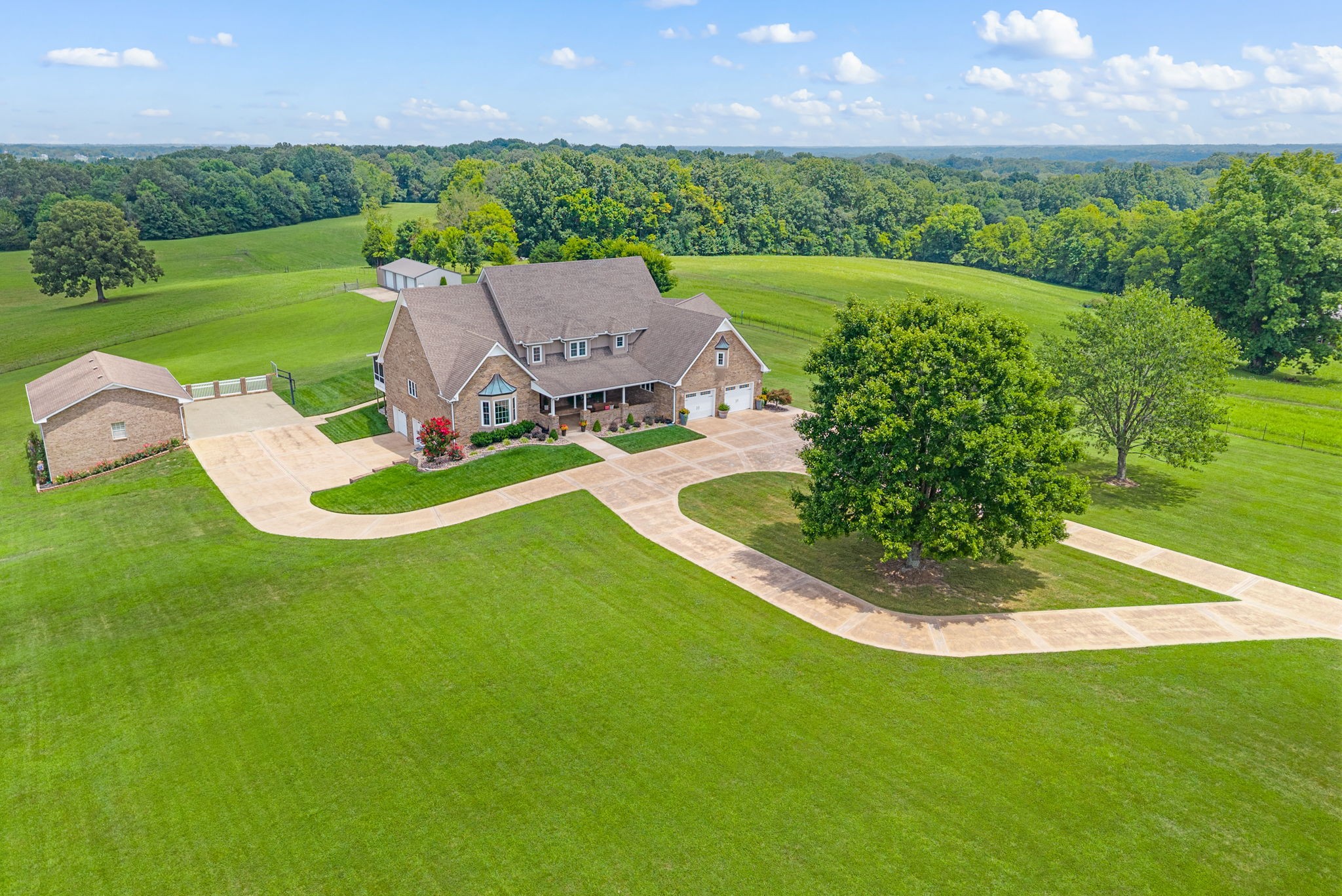 Welcome to 845 McClure Road, a true country estate on 5 acres of gently rolling pasture. This all-brick, two-story home offers nearly 3,900 sq. ft. plus a 1,550 sq. ft. finished basement. A screened deck overlooks the property, while multiple garages provide abundant storage and parking - 7 bays in total. Inside, a grand foyer opens to a main-level office with custom built-ins, a remodeled kitchen with walk-in pantry and island, and a dining room that flows into a bright sunroom. You will notice the main living room features transom windows, a gas fireplace w/ stone hearth and gorgeous wood trim work that flows throughout the entire home. The main-level primary suite includes covered deck access, a jetted tub, double vanity, and walk-in closet.  Upstairs are 3 bedrooms, a Jack & Jill bath, and bonus room. The finished basement adds a full bath, wet bar, and storage rooms perfect for storm shelter use. Outdoor living features a pool house with kitchen and bath, in-ground L-shaped pool with slide, fireplace, and expansive patio. Enjoy an all brick detached garage with 3 bays and walk out door just steps from the house. A 45x25 utility building with bays, water, and electricity adds versatility and extra room for the outdoor enthusiast. There is also a lean to w/ tack room, bring your animals! Convenient to I-24, Fort Campbell, and less than an hour from Nashville. Enjoy no city taxes while living your dream in this country home place.