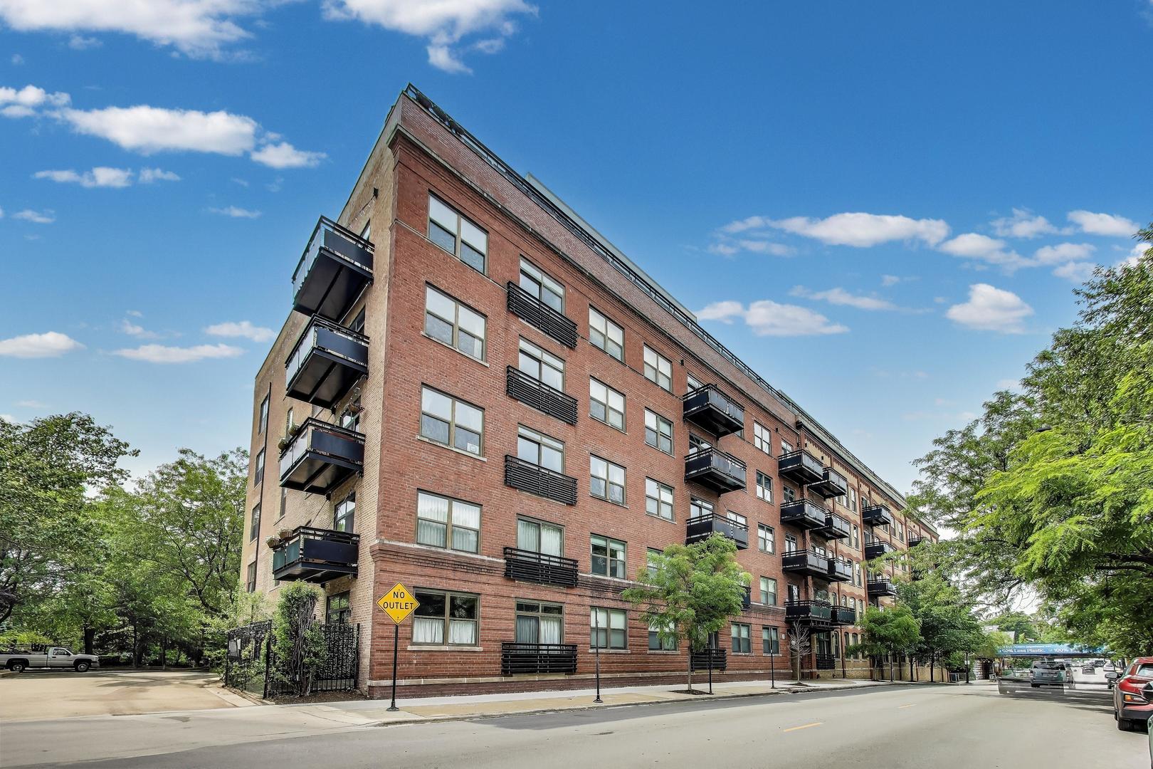 Urban loft living at its finest in this sun-soaked 2-bed, 2-bath condo at Regal Lofts! Tucked away in the quiet rear of the building, this expansive residence features soaring ceilings, exposed timber beams, and oversized south-facing windows that flood the space with natural light. The open-concept layout includes a large living/dining area with a cozy fireplace and direct access to a private balcony-perfect for entertaining or relaxing al fresco. The stylish kitchen offers granite countertops, breakfast bar seating, and stainless steel appliances. Split bedroom layout ensures privacy, and both bedrooms feature generous closet space and plush carpeting. Two deeded exterior parking spaces are included in the price!  Enjoy the convenience of in-unit laundry, central air, and modern touches like hardwood floors and double-sink vanities. Located in a well-managed elevator building with fitness center and additional storage. Just steps to the Diversey bus, and close to parks, Costco, Starbucks, Whole Foods, restaurants, and easy access to the highway.