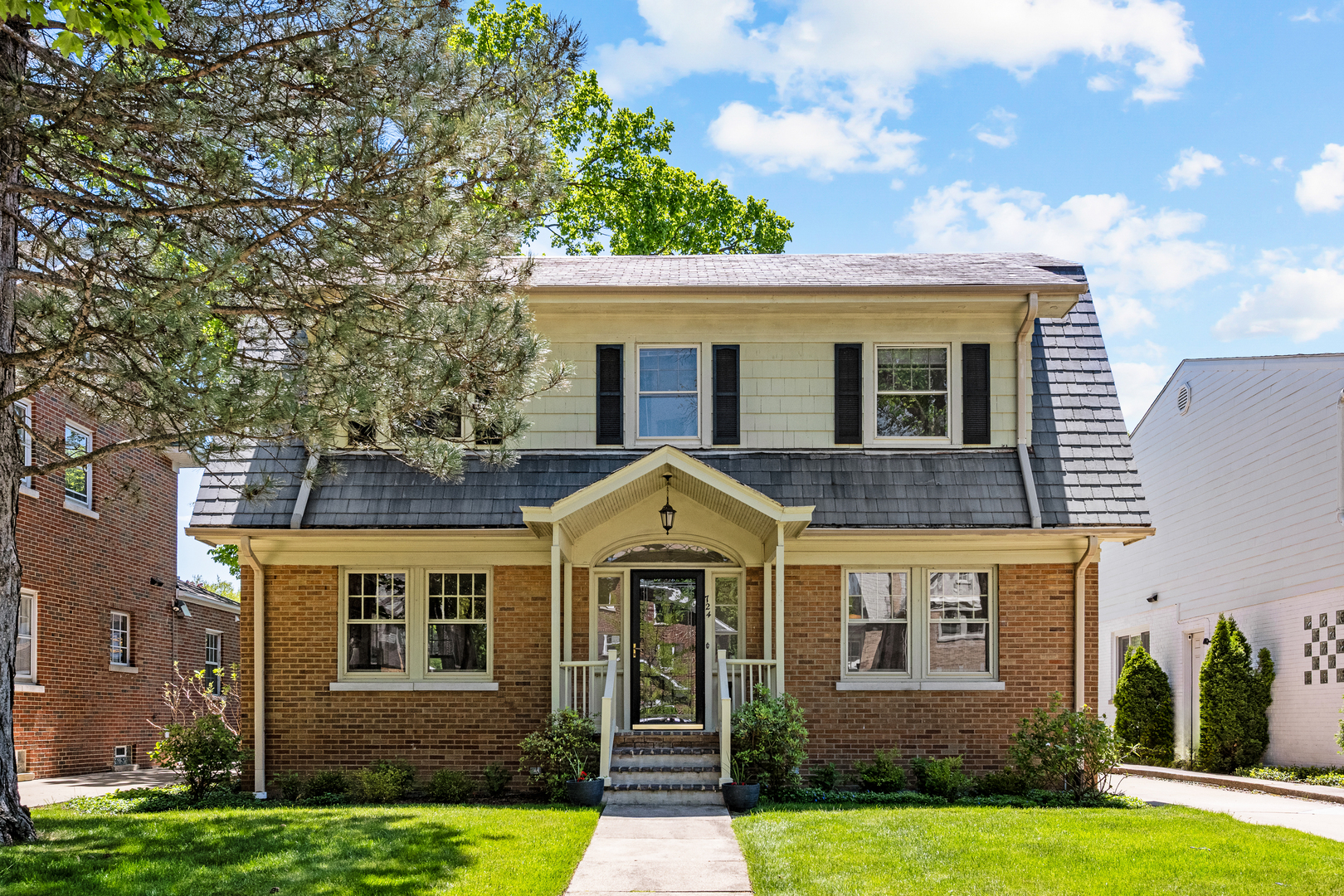 This distinctive center-entrance brick Dutch Colonial is located on a quiet, tree-lined street near the lake, train, and local schools.    The main level features a spacious entryway leading to a living room with a wood-burning fireplace and built-in bookshelves. The floor plan includes a formal dining room with built-in corner hutches and a kitchen that opens to a south-facing family room.    The second floor offers a primary bedroom with a walk-in closet and an additional closet space. Two good-sized bedrooms and a tandem room provide flexible space. The tandem room can serve as a fourth bedroom. The lower level includes a recreation room and plenty of storage. The property is complete with an oversized two-car garage and a landscaped yard.